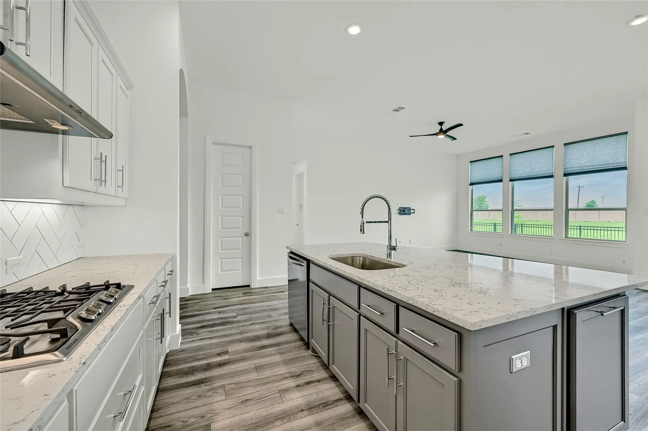 Kitchen with a sink, gray cabinets, stainless steel appliances, wood finished floors, and under cabinet range hood