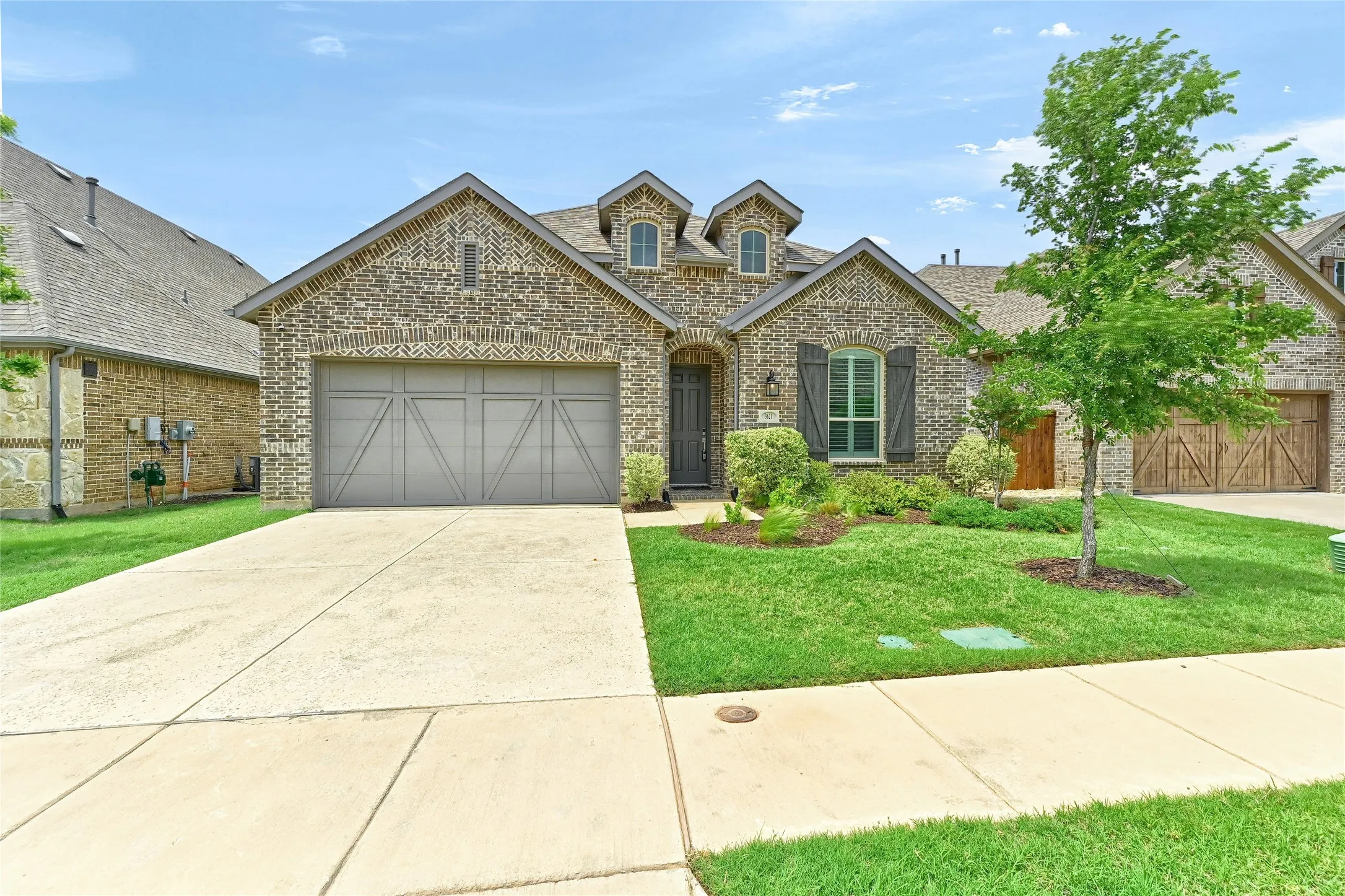 French provincial home with a shingled roof, brick siding, a garage, a front yard, and driveway