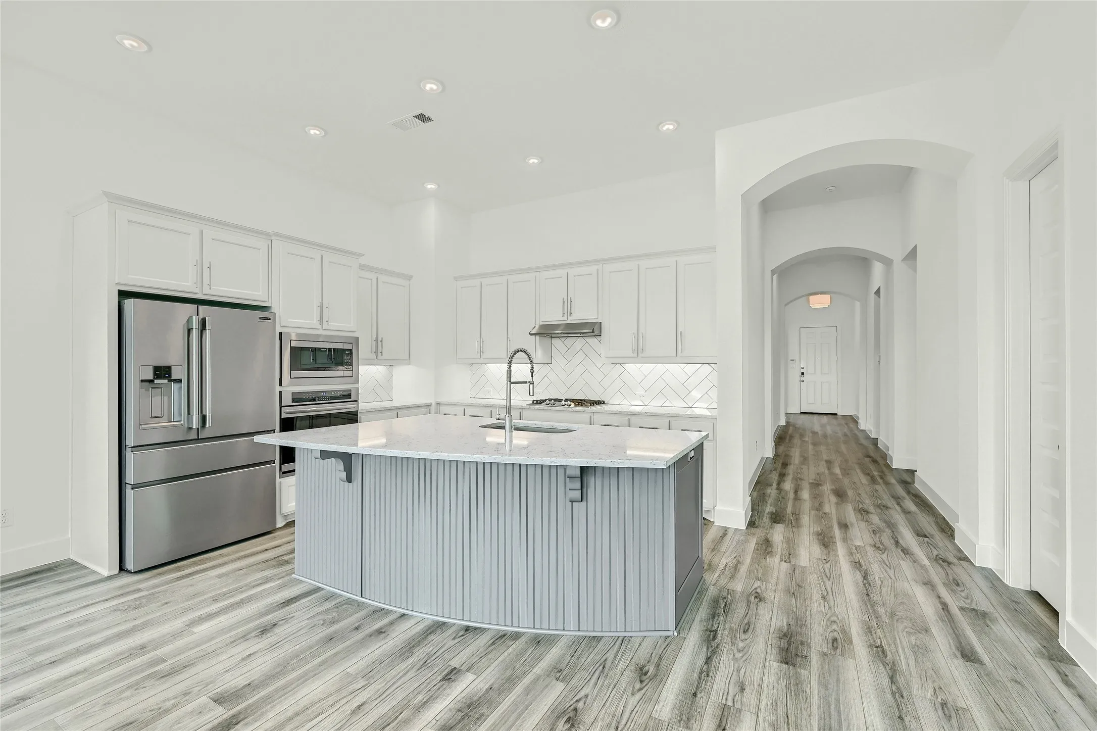 Kitchen featuring appliances with stainless steel finishes, light wood-style floors, light countertops, arched walkways, and visible vents