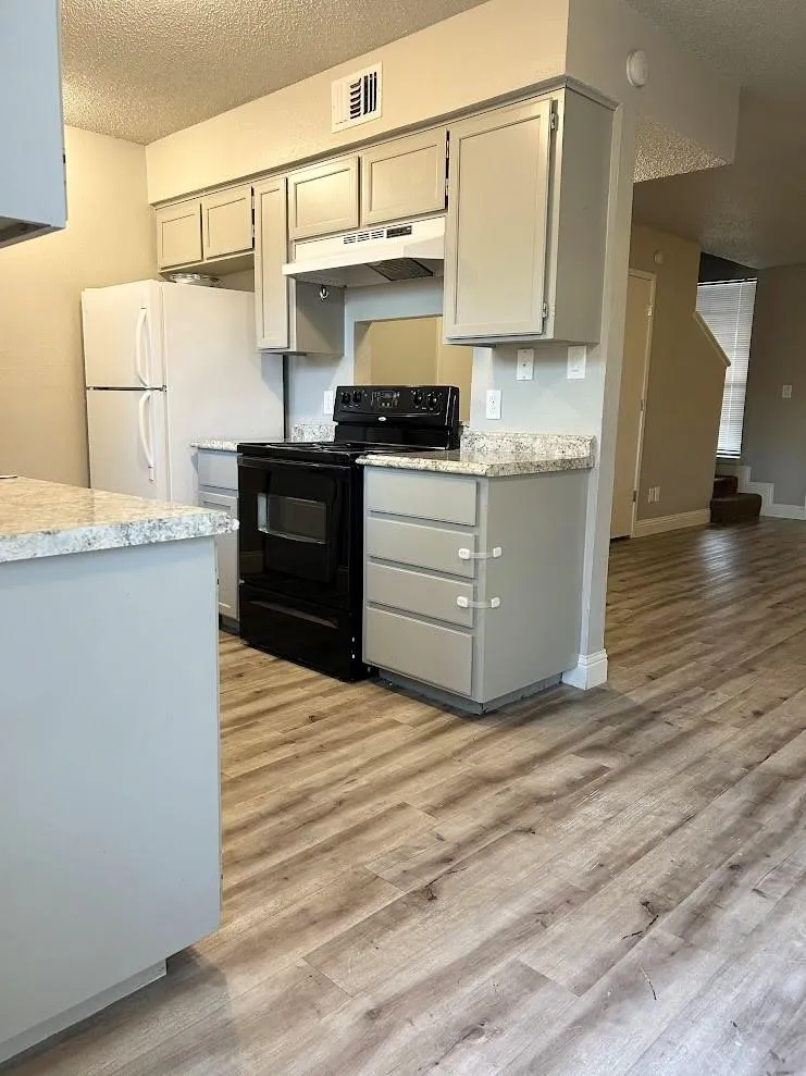 Kitchen featuring light gray cabinetry, a black electric range, a white refrigerator, light-toned countertops, and wood-finish flooring