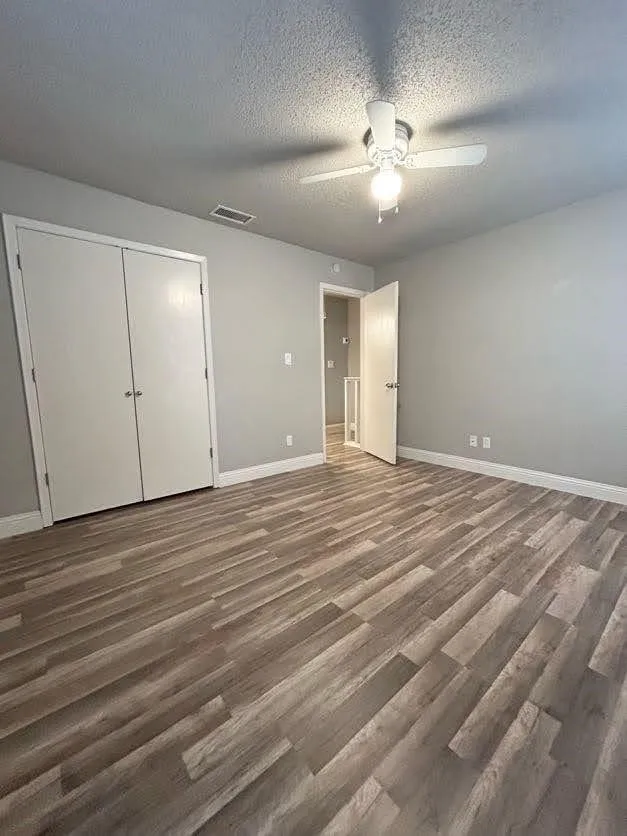 Spacious room featuring wood-finish flooring, a ceiling fan with integrated lighting, and neutral wall tones