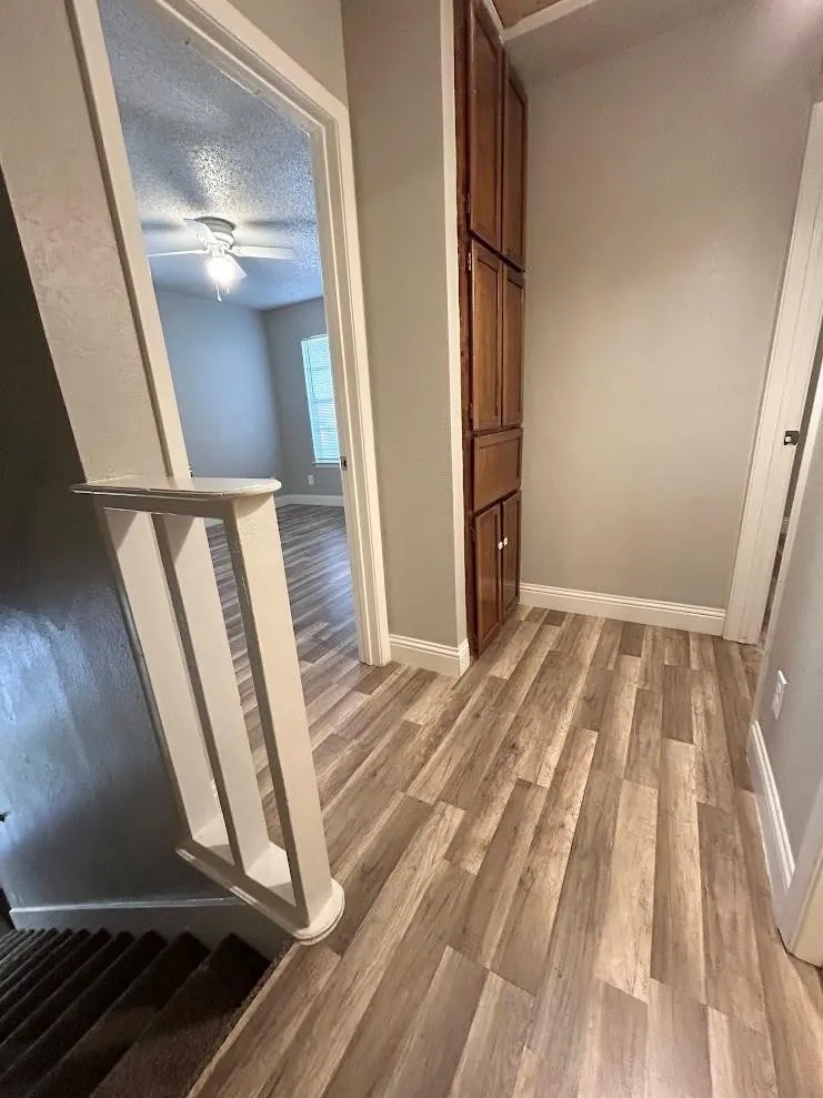 Hallway featuring wood-look plank flooring, built-in storage cabinetry, white baseboards, and a view into a room with a ceiling fan and window