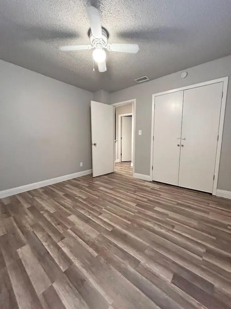 Interior room featuring wood-finish flooring, light gray wall paint, a ceiling fan with integrated lighting, and two white bi-fold closet doors