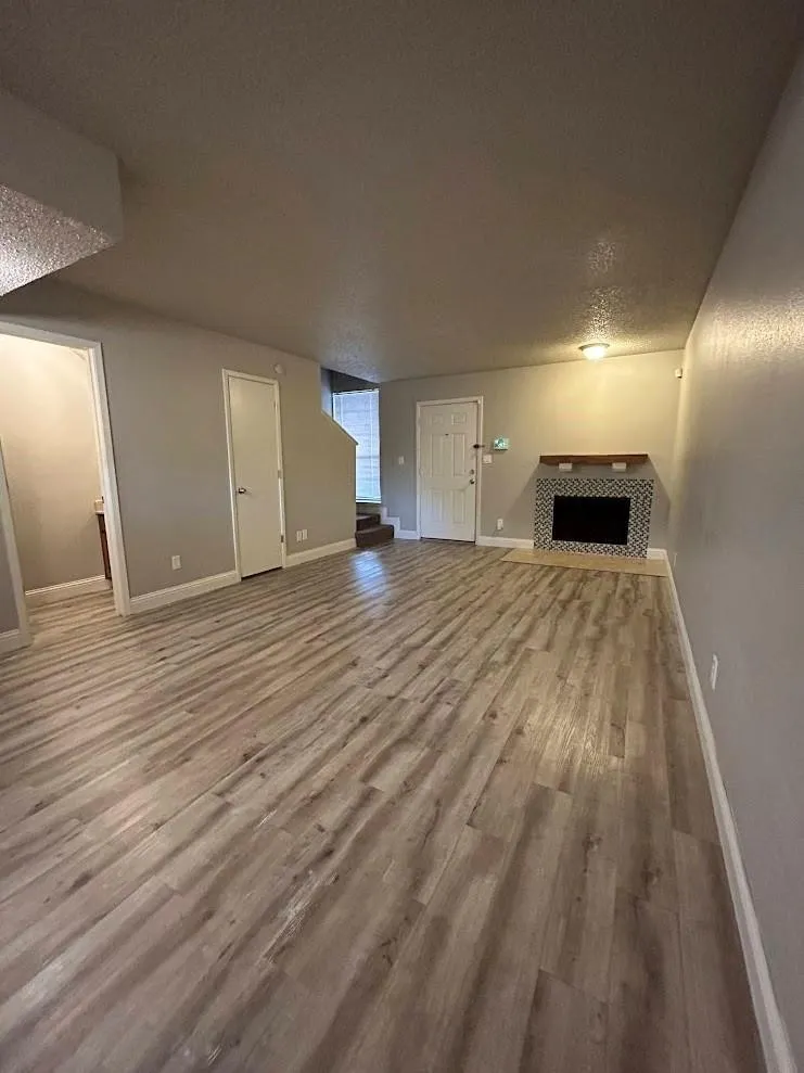 Spacious living area featuring wood-finish flooring, a fireplace with a decorative tile surround, and light gray wall finishes