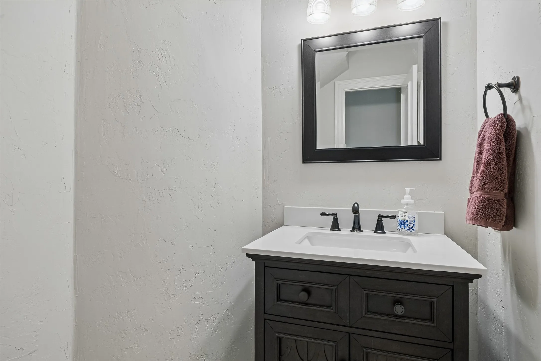 Vanity area featuring a dark wood cabinet with an integrated sink, white countertop, and matte black fixtures