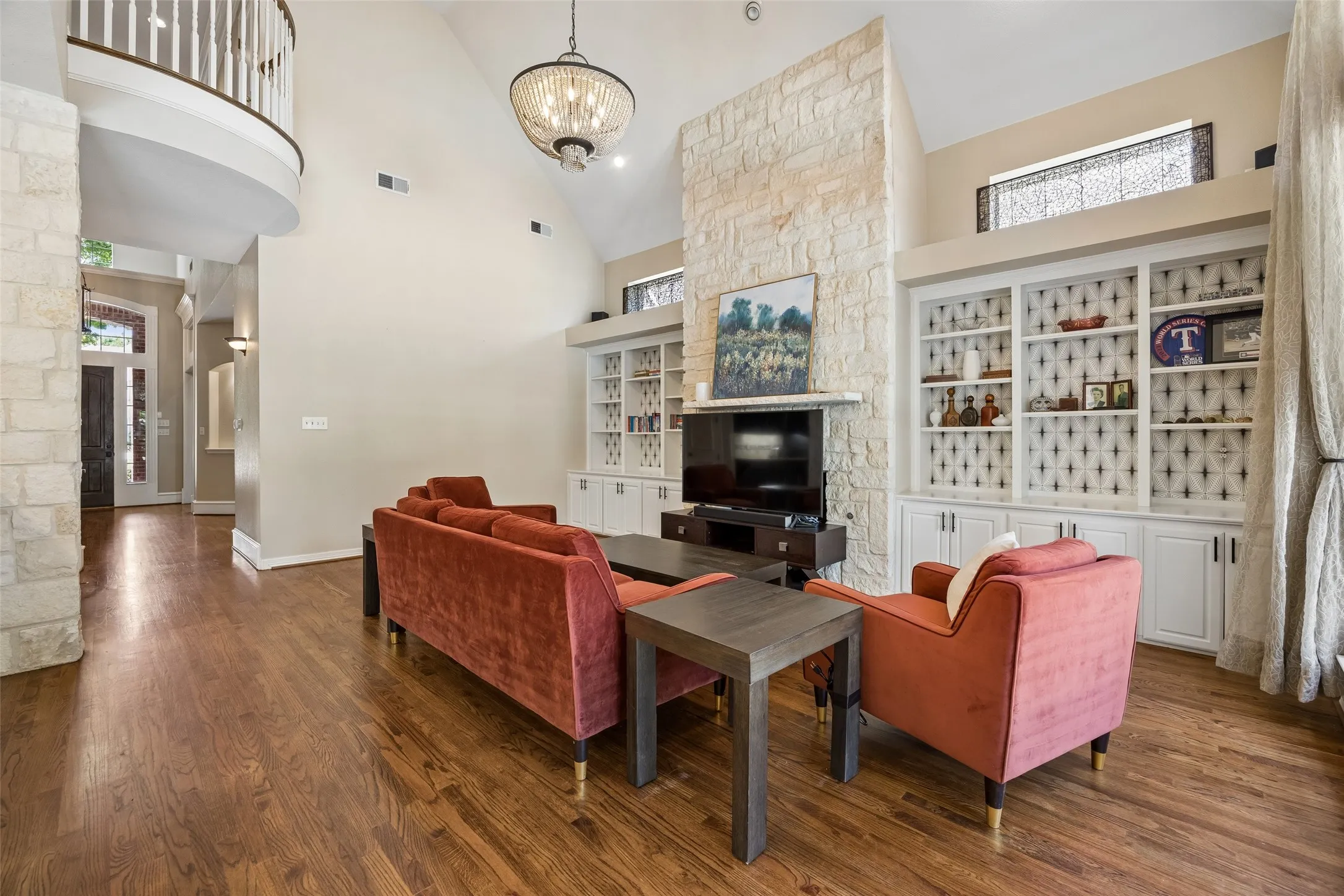 Spacious living area featuring high ceilings, wood-finish flooring, a stone-clad fireplace, and integrated custom shelving