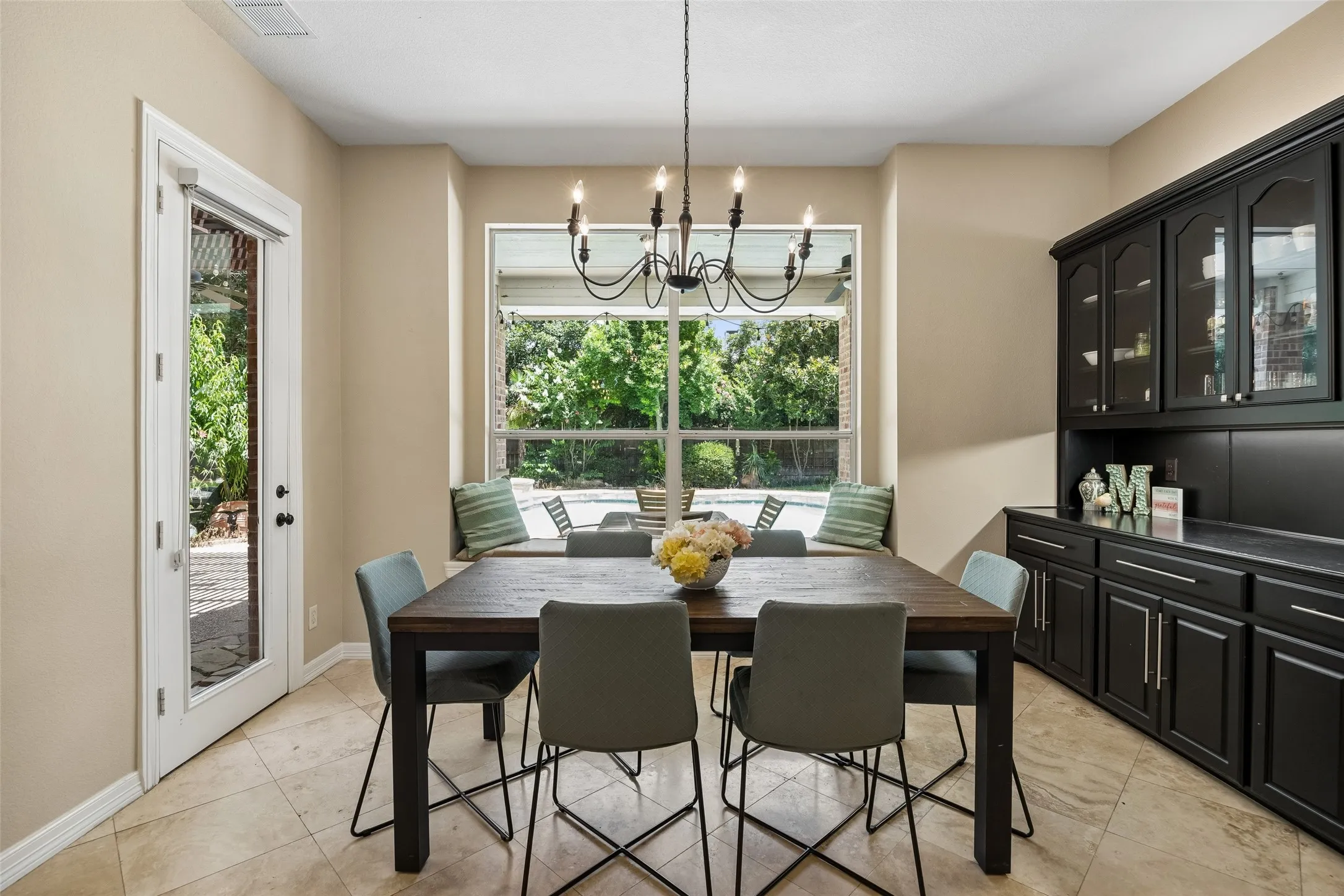 Dining space featuring a large window with a built-in window seat, a glass-paned door, tiled flooring, and a dark wood-finish dining table