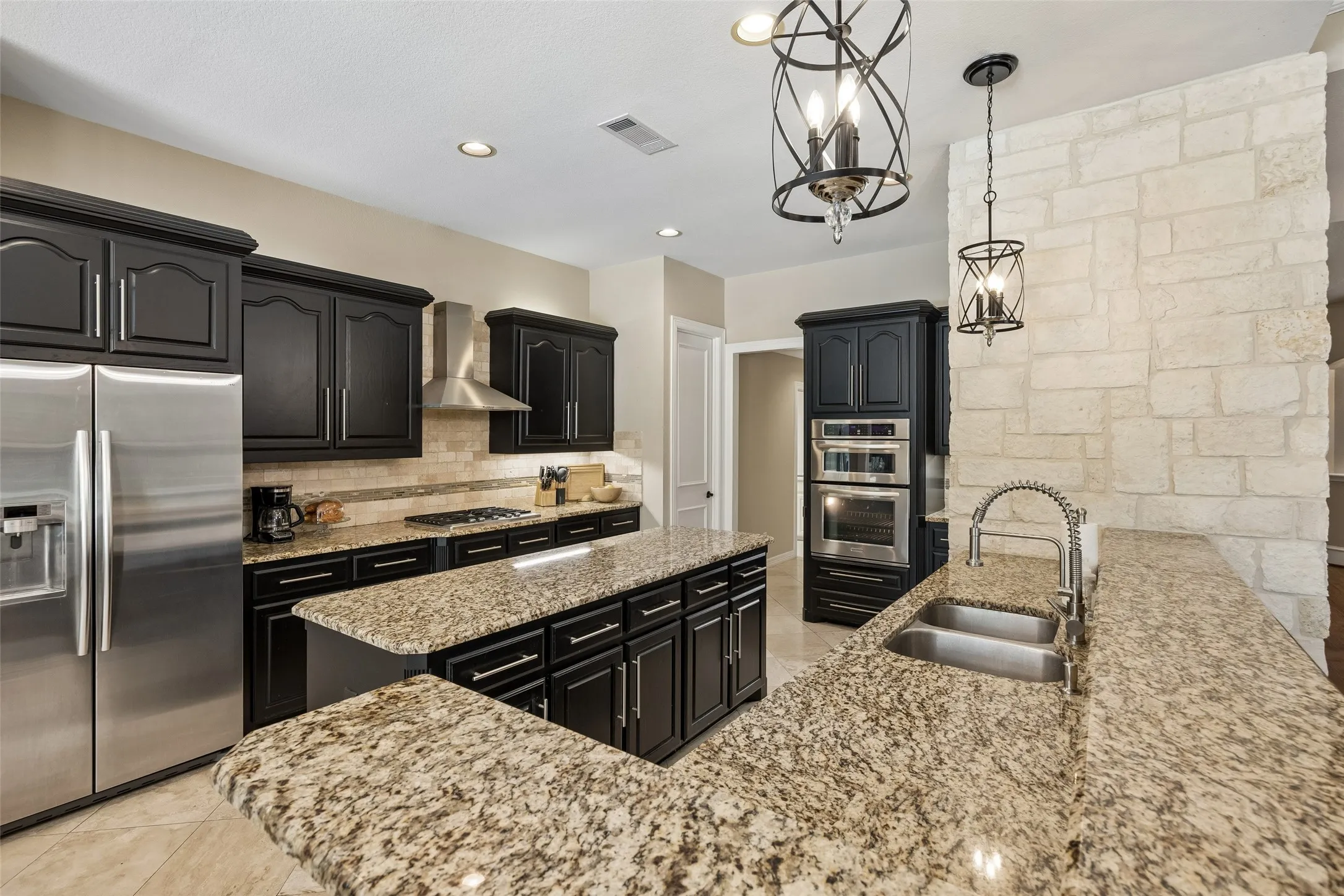 Kitchen featuring granite countertops, dark wood cabinetry, a built-in stainless steel double oven, a stainless steel refrigerator, and a stone accent wall