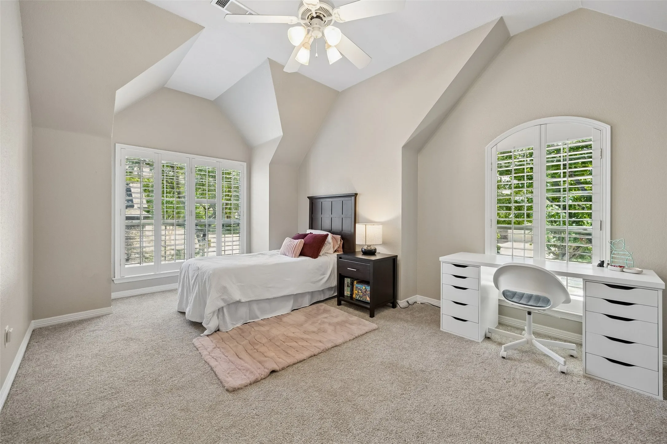 Spacious room featuring vaulted ceilings, light-colored carpeting, a ceiling fan, and multiple windows with plantation shutters