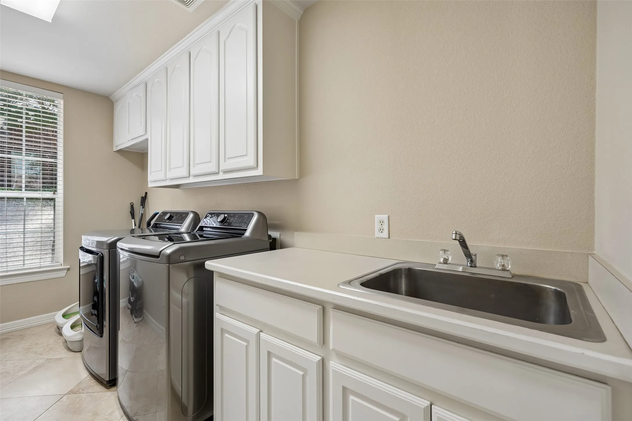 Utility room featuring extensive white cabinetry, a built-in stainless steel sink, light-toned countertops, and neutral wall paint