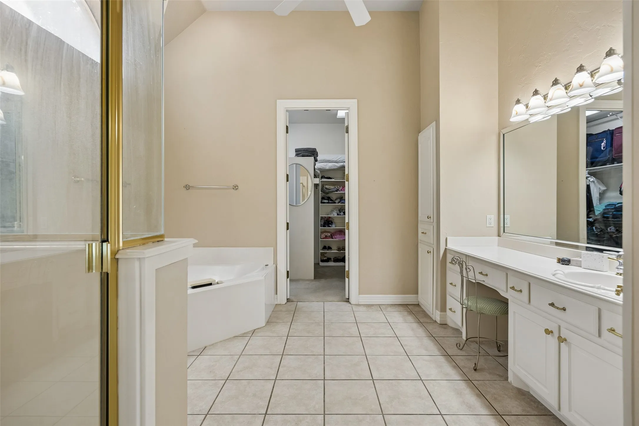Spacious bathroom featuring tiled flooring, a built-in corner tub, and a shower enclosure with gold-tone framing