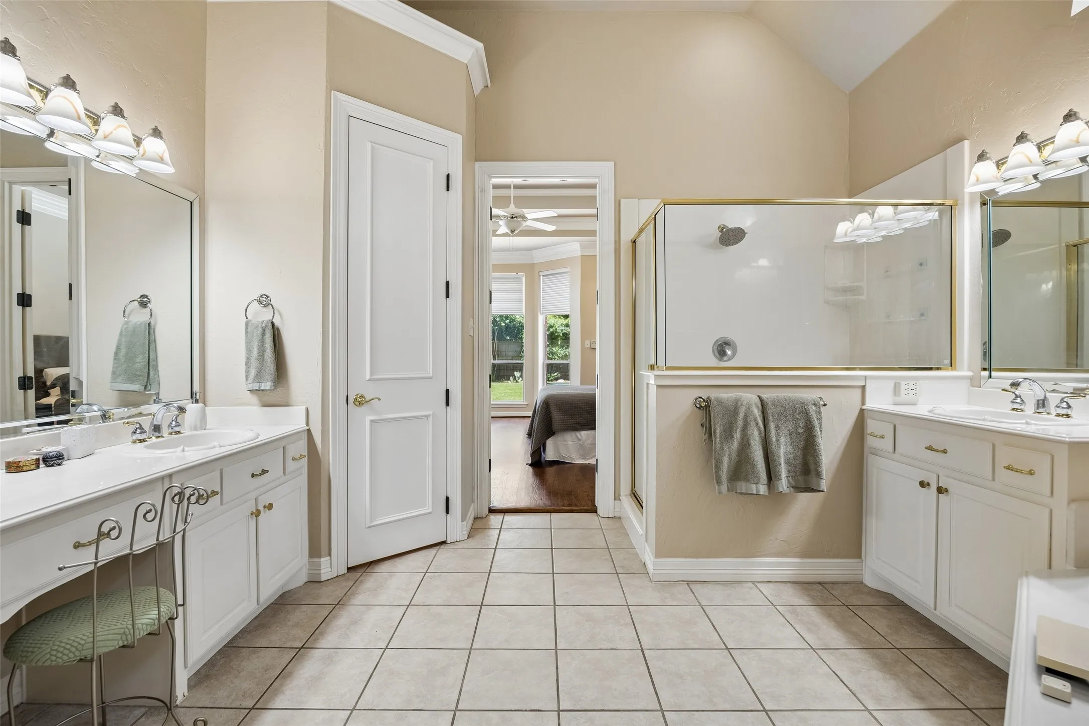 Bathroom featuring dual vanity areas, a glass-enclosed shower, white cabinetry, and light-toned tile flooring