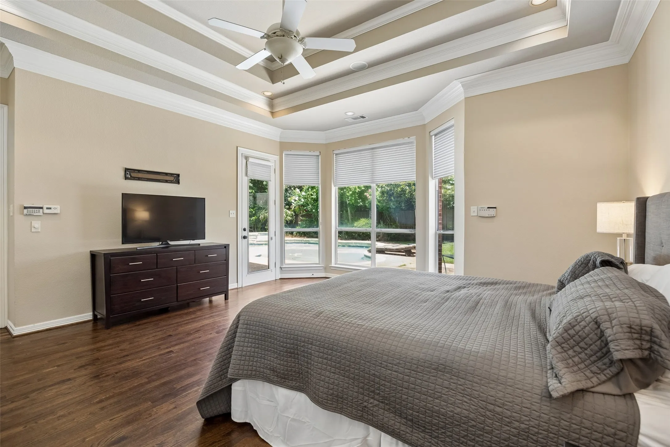 Room featuring wood-finish flooring, a tray ceiling with a ceiling fan, and large windows with blinds