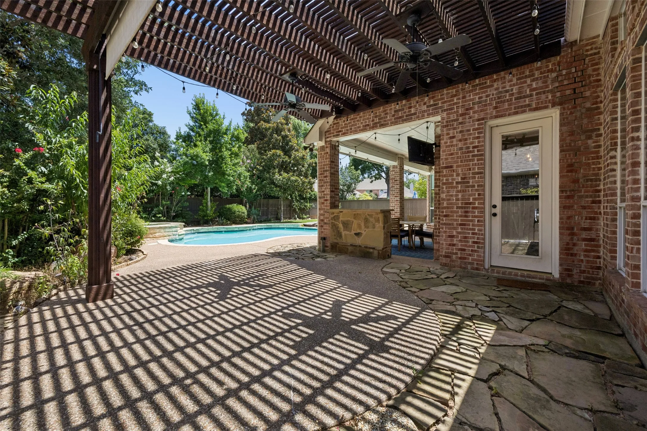 Outdoor living space featuring a wood pergola with ceiling fans, a flagstone patio, a brick exterior, and a swimming pool