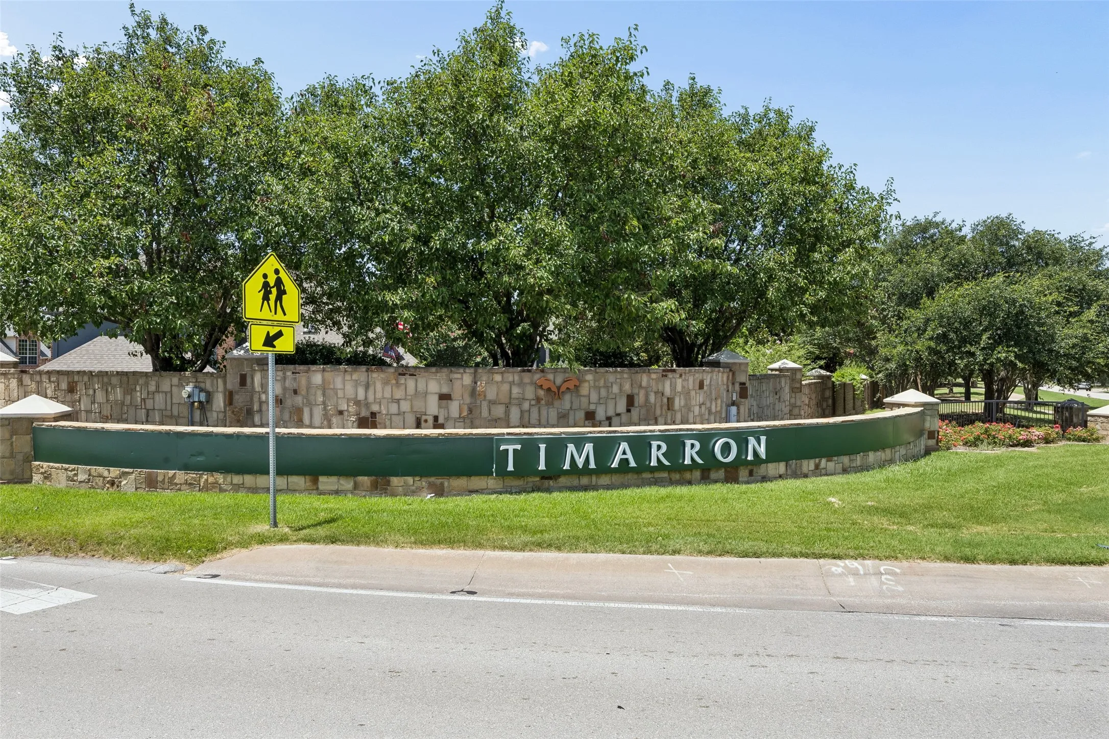 Timarron community entrance featuring a stone wall with integrated signage, mature trees, and manicured green spaces