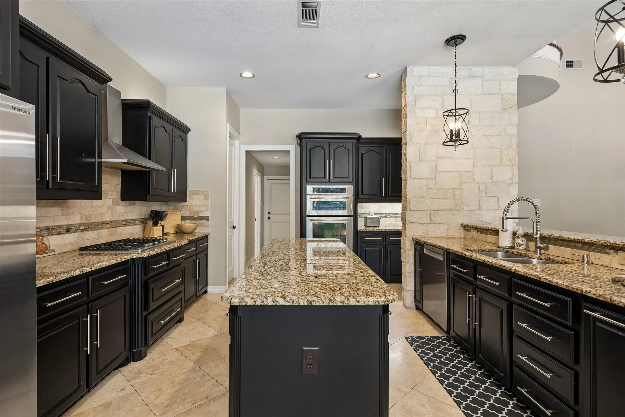 Well-appointed kitchen featuring granite countertops, dark cabinetry, stainless steel appliances, a center island, and stone accent wall