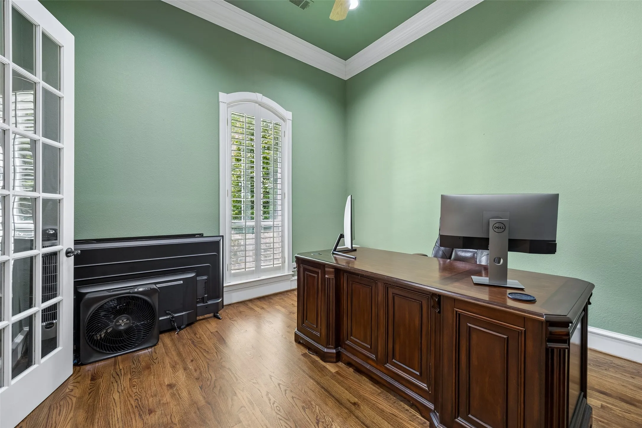Room featuring wood-finish flooring, French doors with glass panes, and a tall arched window with plantation shutters