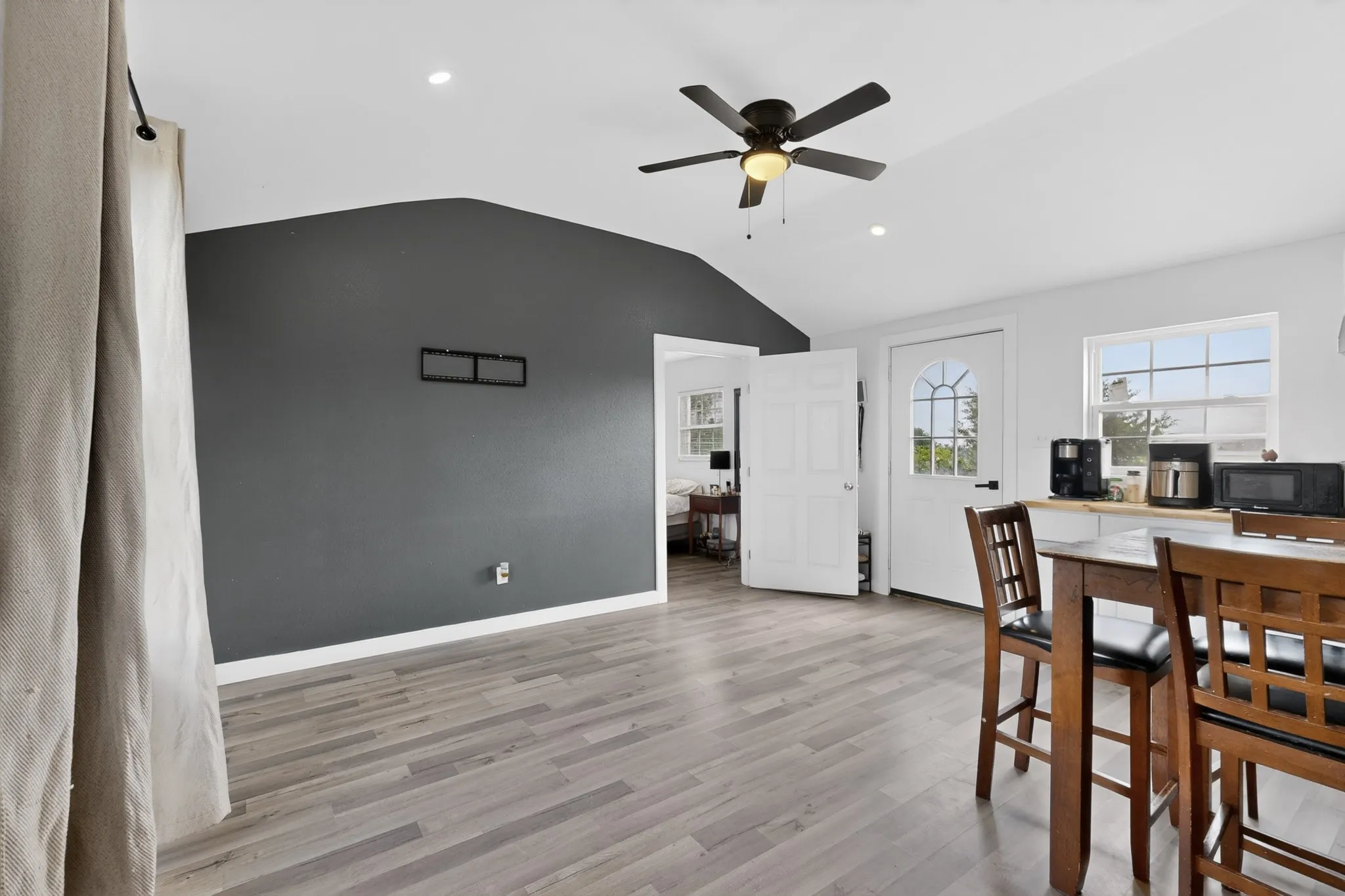Open-concept living area featuring wood-finish flooring, a vaulted ceiling with recessed lighting, and a dark-painted accent wall