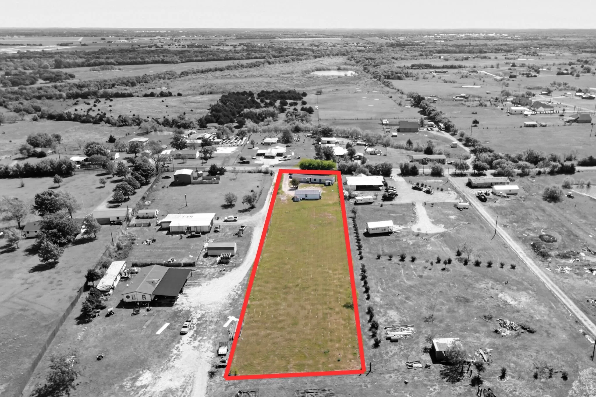 Property parcel featuring an elongated grassy area bordered by a red outline, with a single-story residence and outbuilding positioned at one end