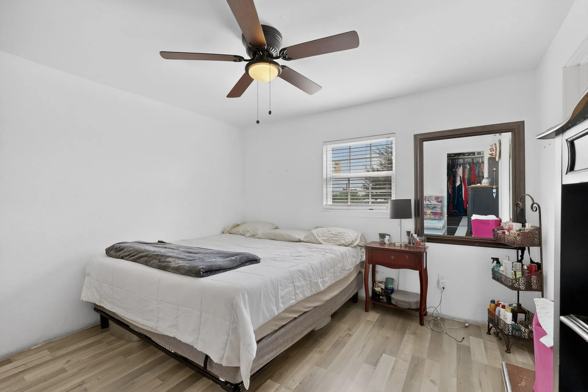 Spacious room featuring wood-finish flooring, a ceiling fan with integrated lighting, and a window with horizontal blinds