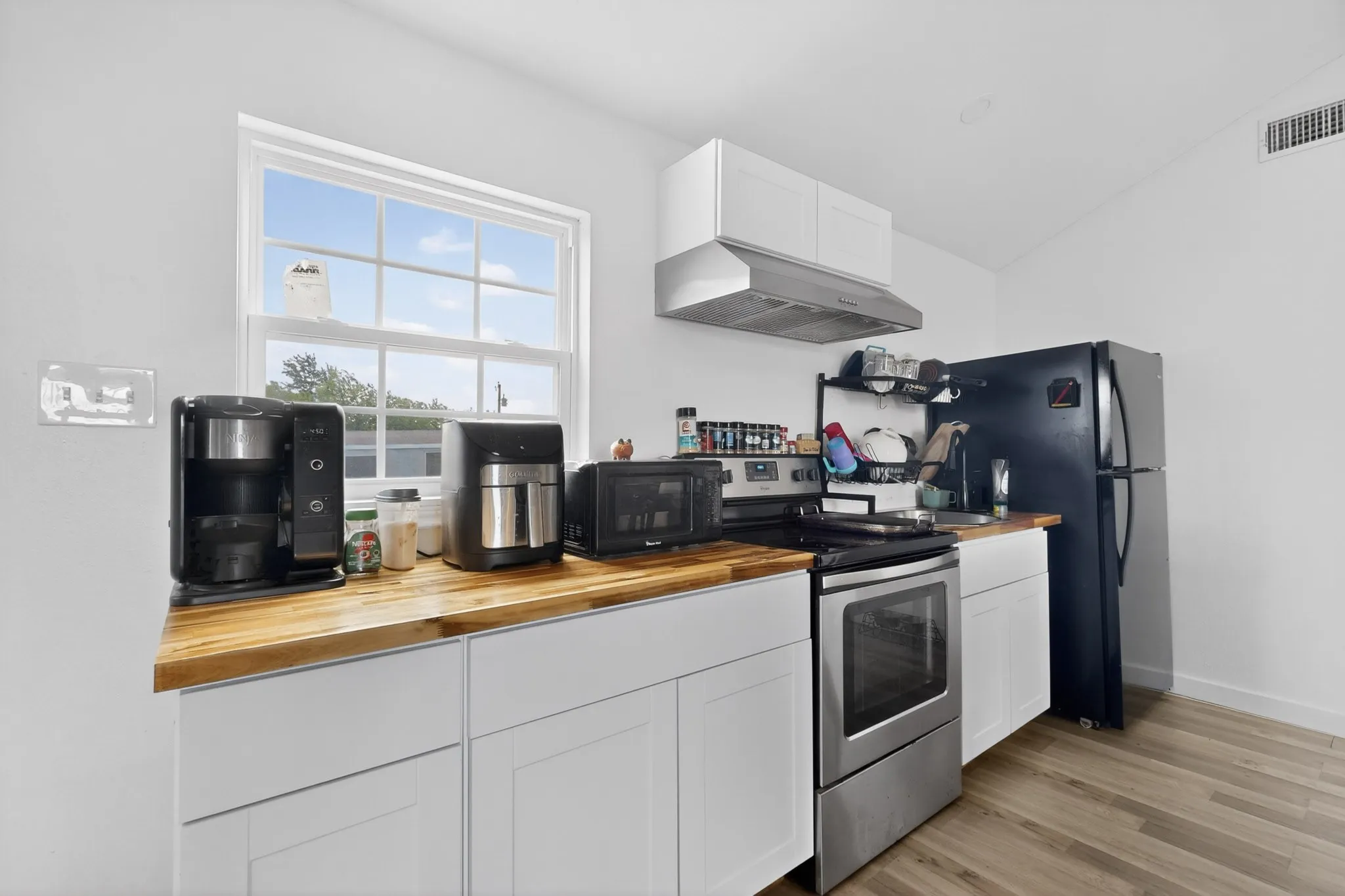 Kitchen featuring white cabinetry, wood-finish countertops, stainless steel oven, and a window providing natural light
