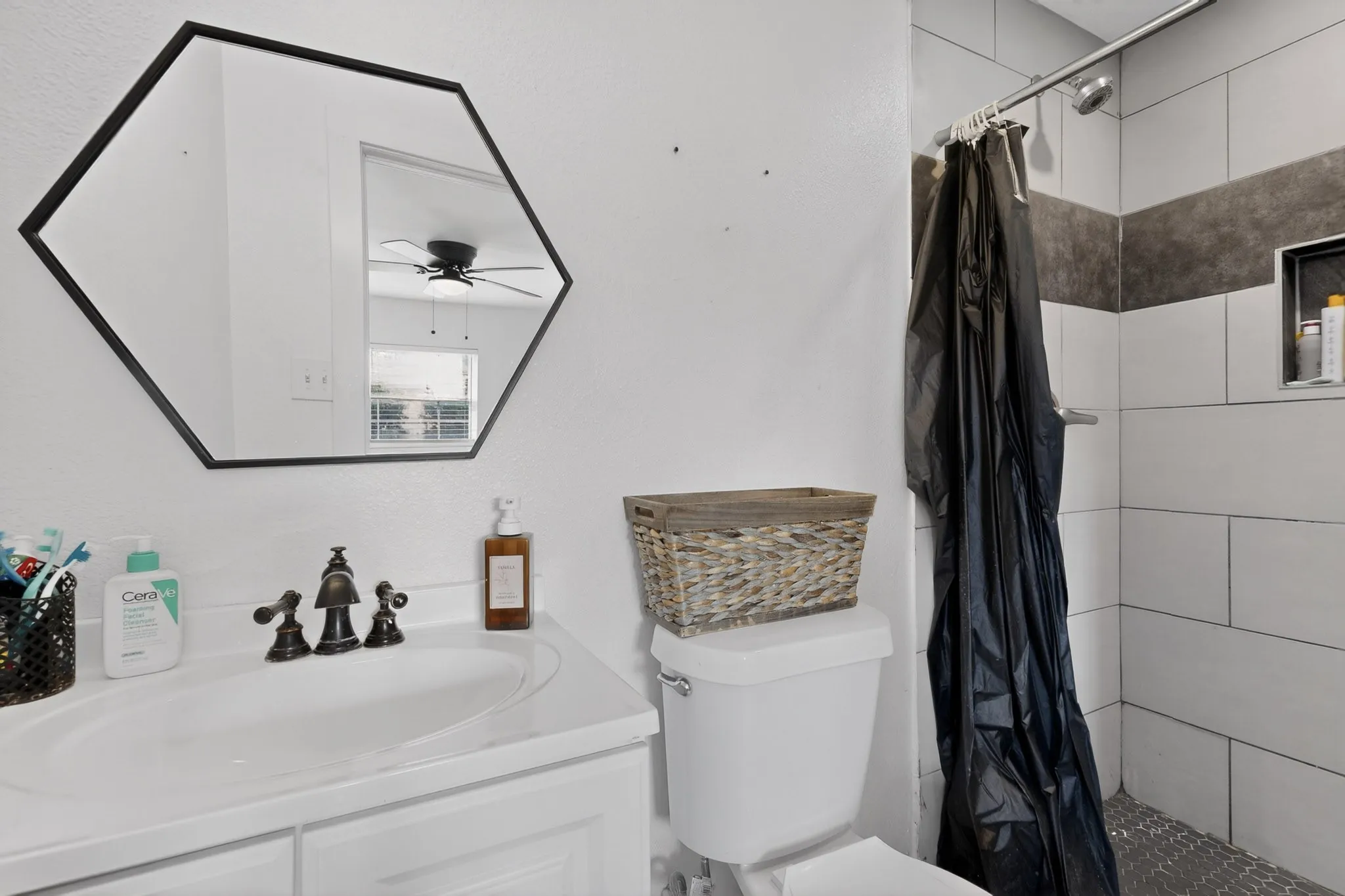 White vanity with integrated sink, oil-rubbed bronze faucet, and black hexagonal mirror