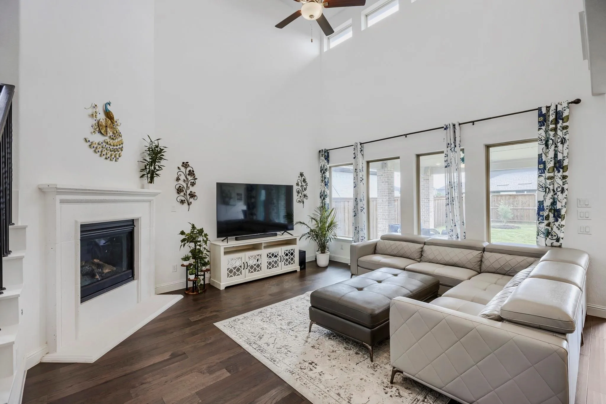 Living area featuring high ceilings, dark wood-finish flooring, a contemporary fireplace with a white mantel, and a wall of windows providing natural illumination