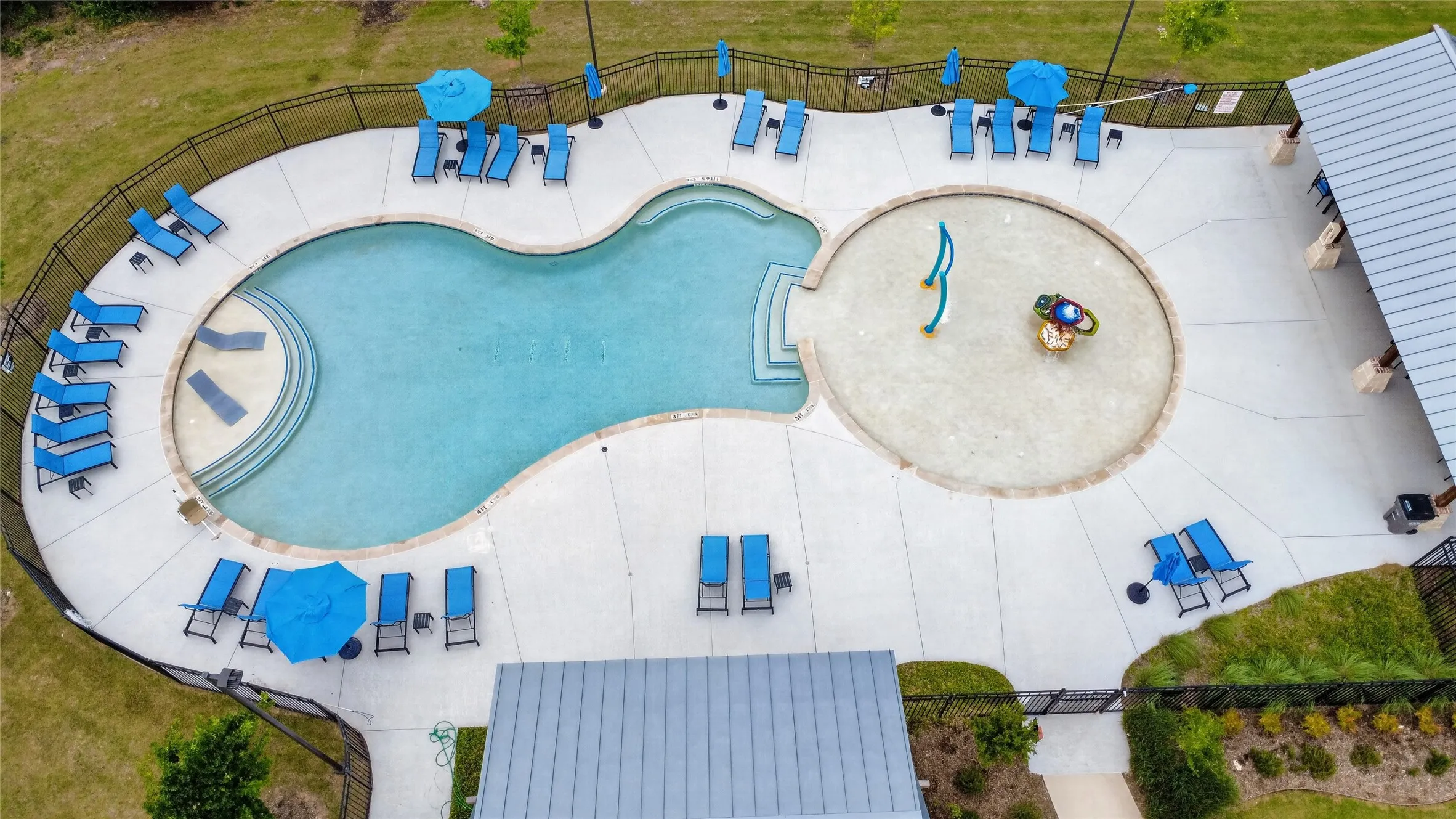 Resort-style community  pool area featuring a freeform swimming pool with tiered entry steps, an adjacent circular splash pad, and surrounding concrete decking