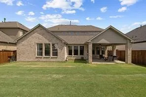 Expansive backyard featuring a covered patio, brick exterior, multiple large windows, and a privacy fence