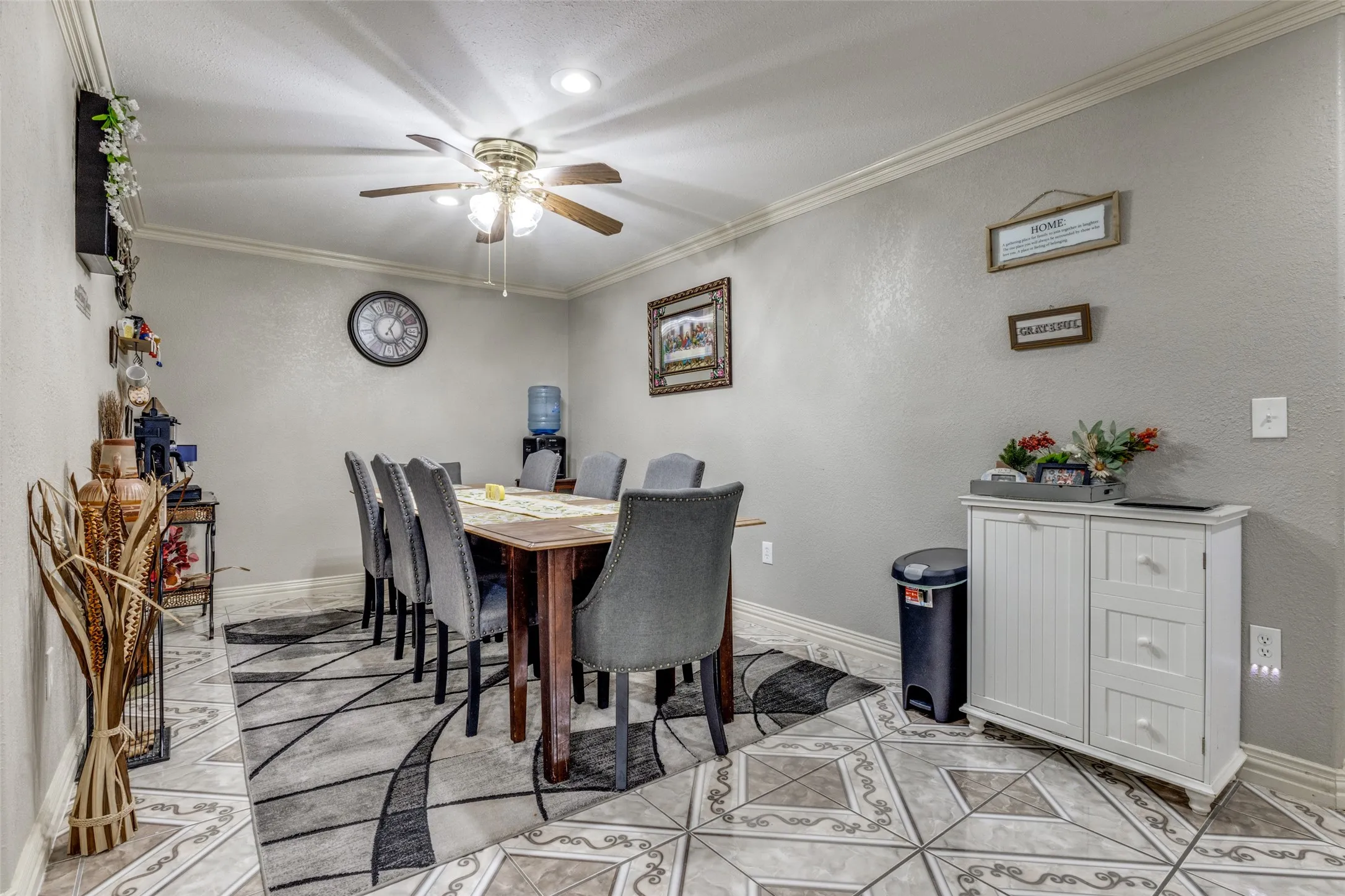 Dining space with ornamental molding, a textured wall, ceiling fan, and light tile patterned floors