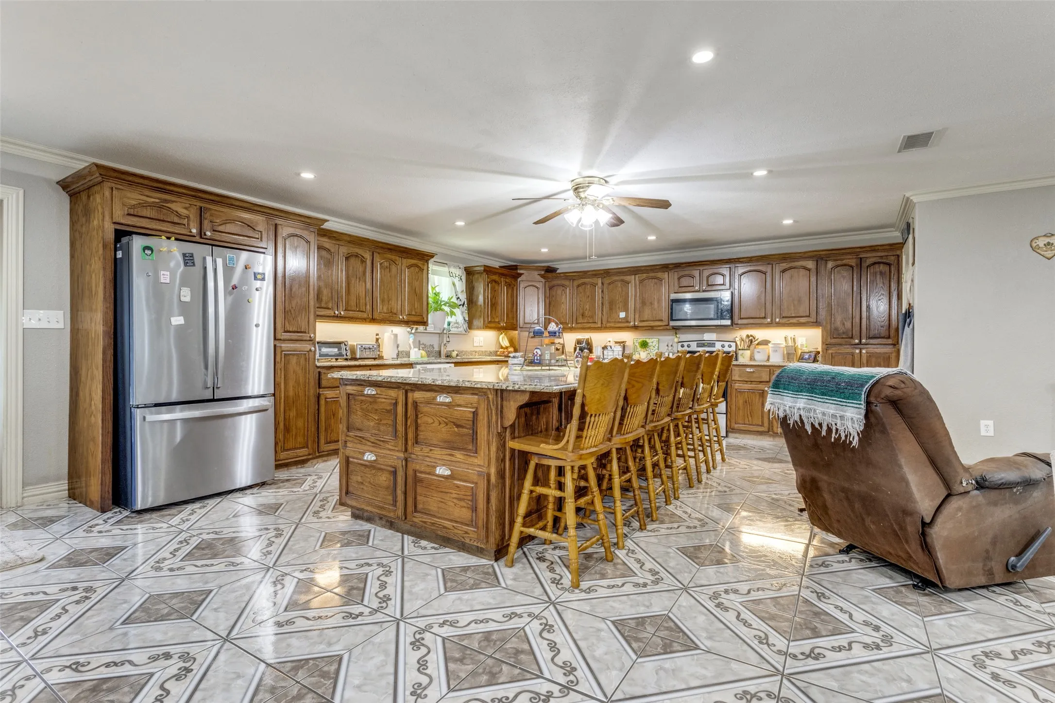 Kitchen with brown cabinetry, recessed lighting, crown molding, light stone countertops, and stainless steel appliances