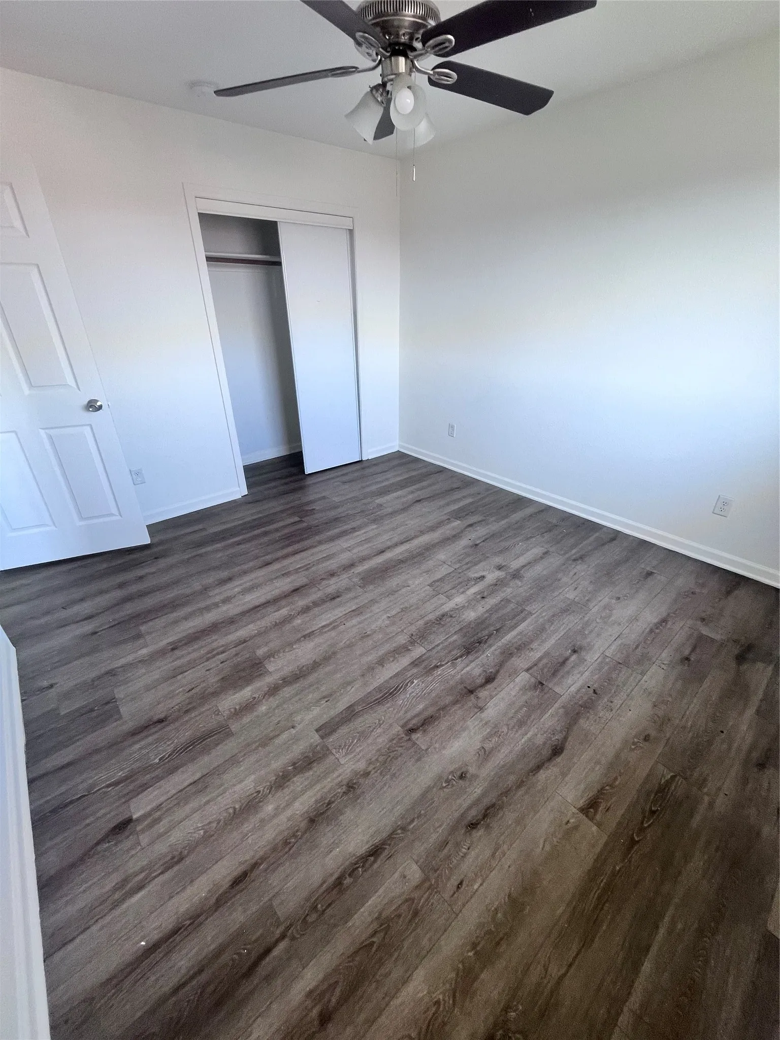 Bedroom featuring wood-finish flooring, a ceiling fan with integrated lighting, and a closet with sliding doors