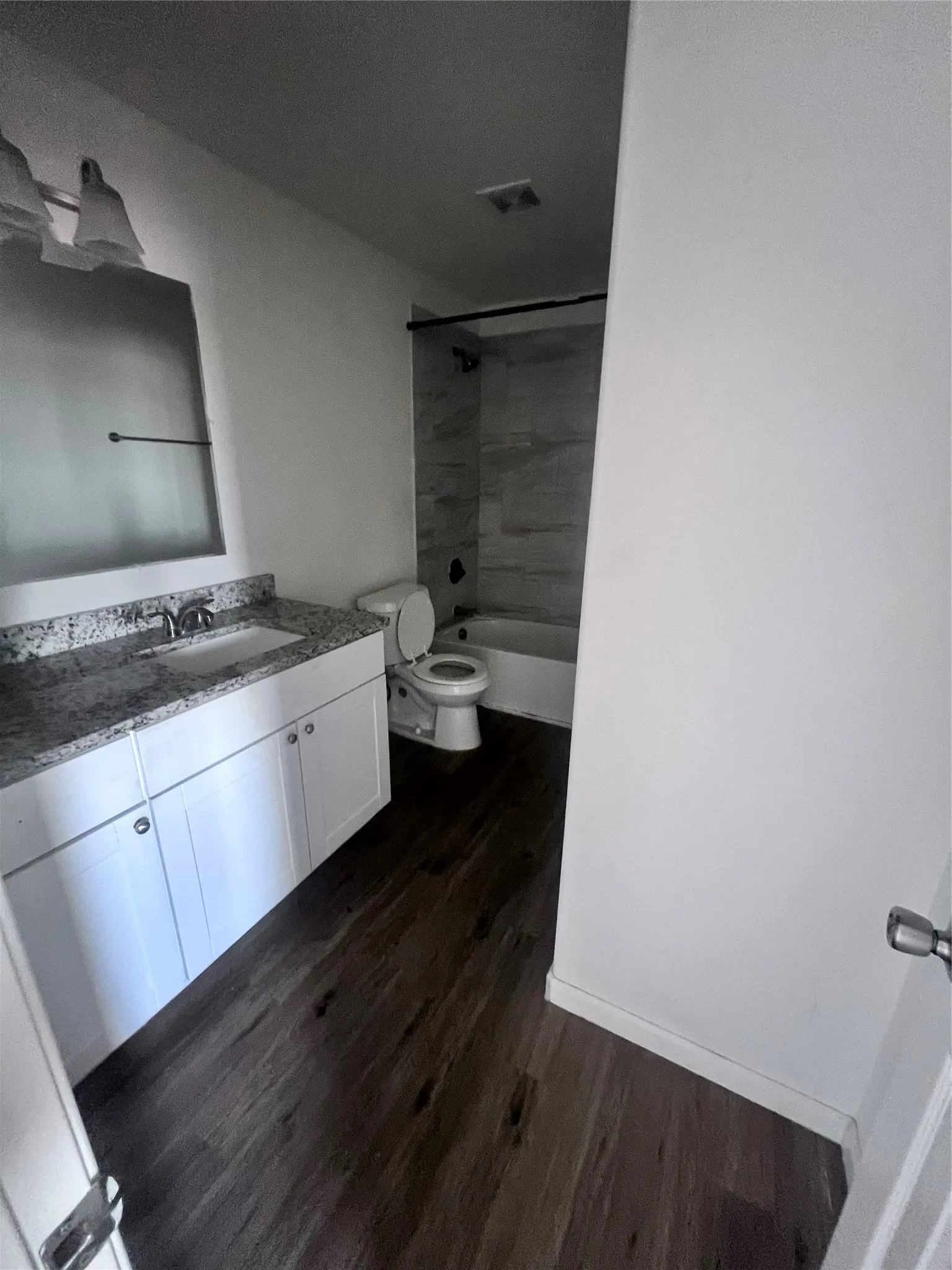 Bathroom featuring a white vanity with a granite-style countertop and undermount sink, wood-finish flooring, and a bathtub with tiled surround