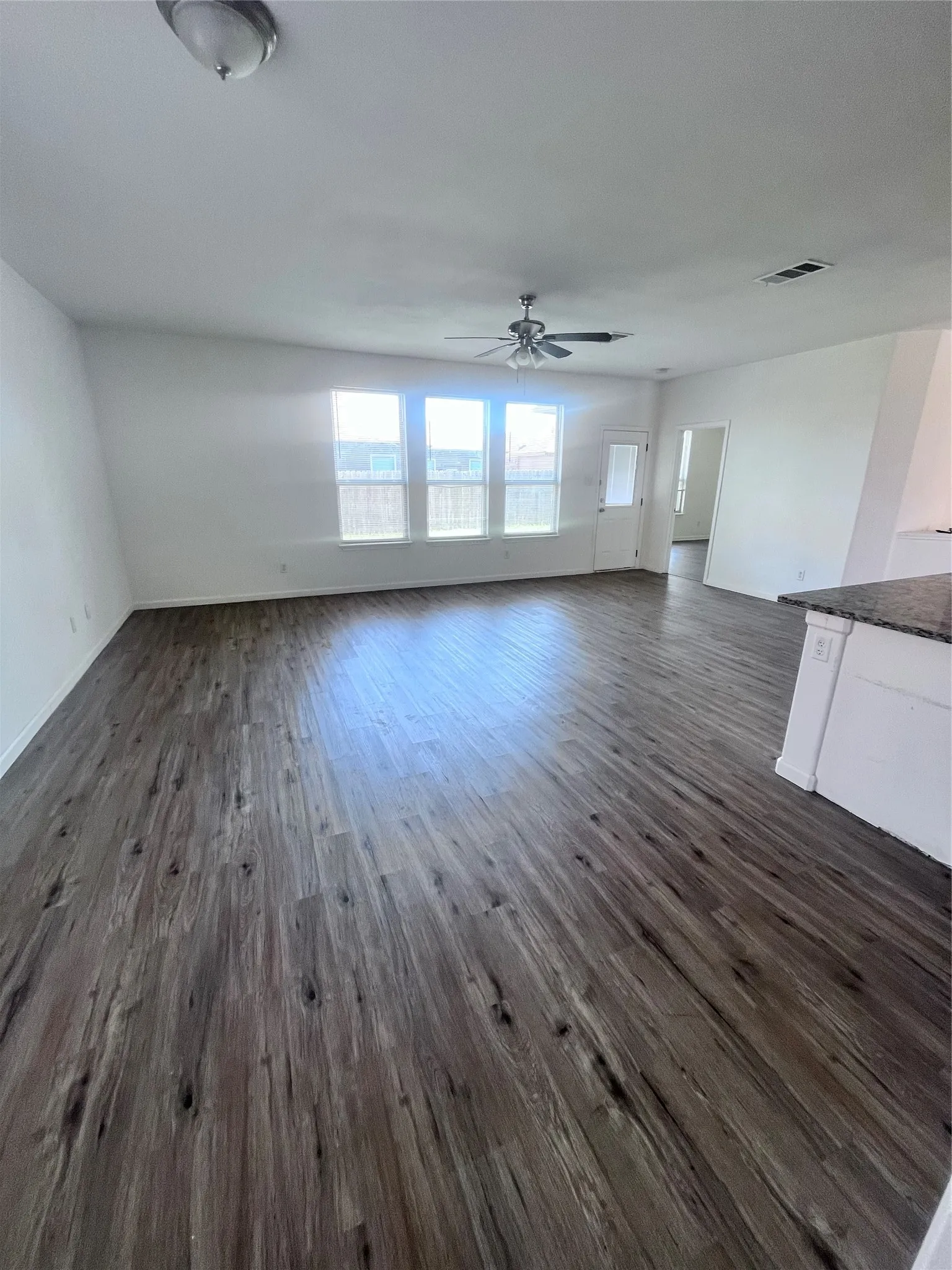 Spacious room featuring wood-finish flooring, a contemporary ceiling fan, and a trio of windows providing ample natural light