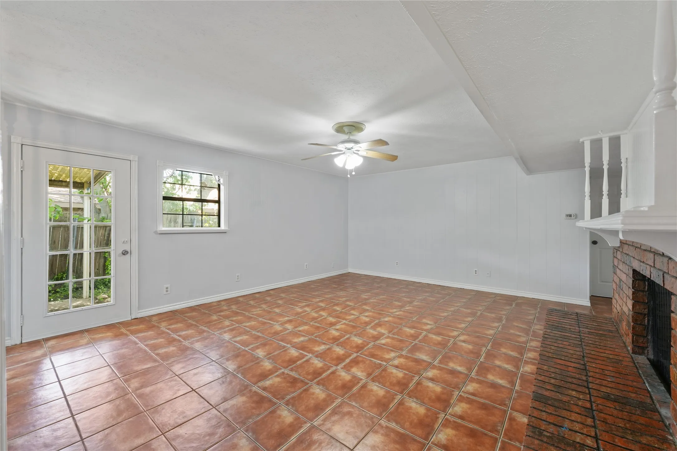 Unfurnished living room featuring a brick fireplace, ceiling fan, and tile flooring