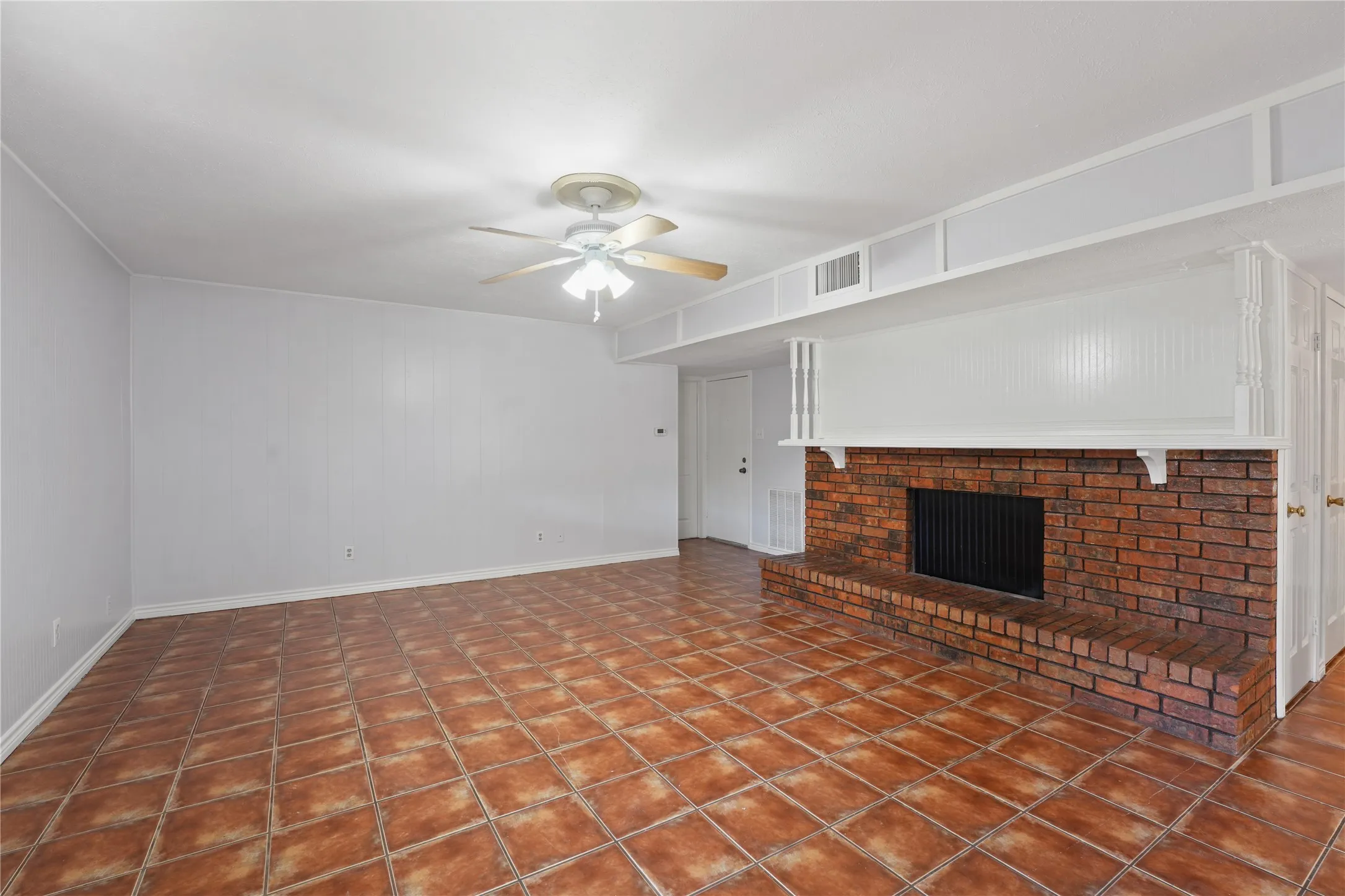 Unfurnished living room with dark tile flooring, a brick fireplace, and ceiling fan