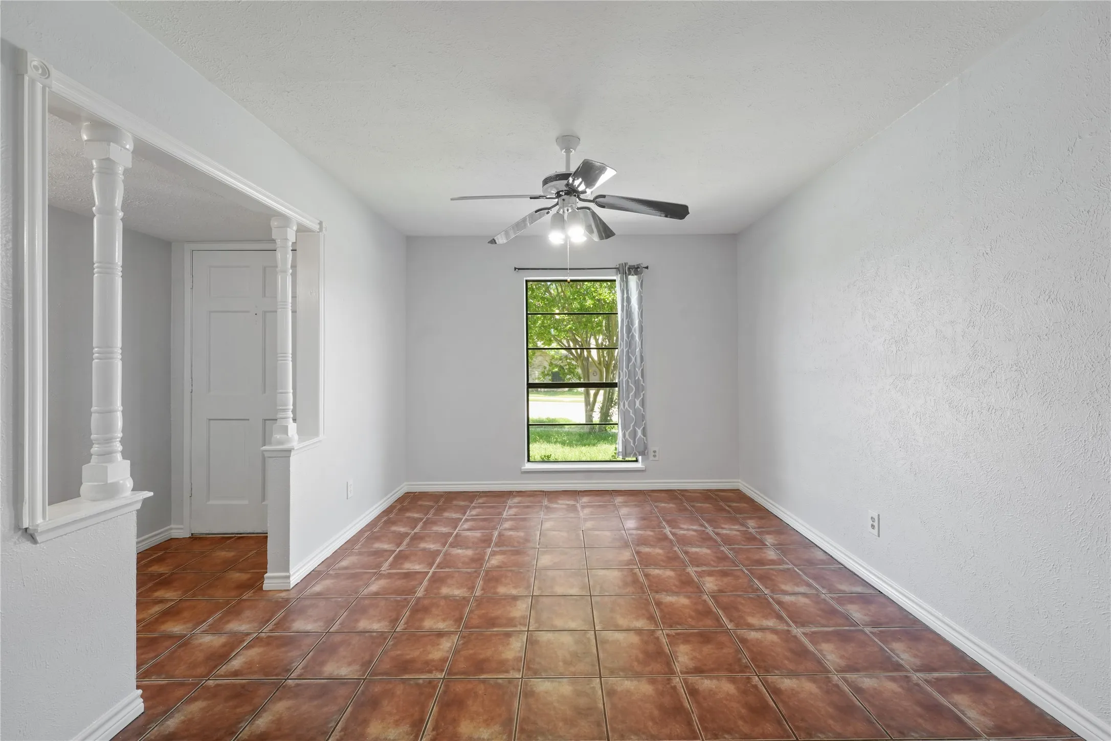 Unfurnished room with dark tile floors, ornate columns, and ceiling fan