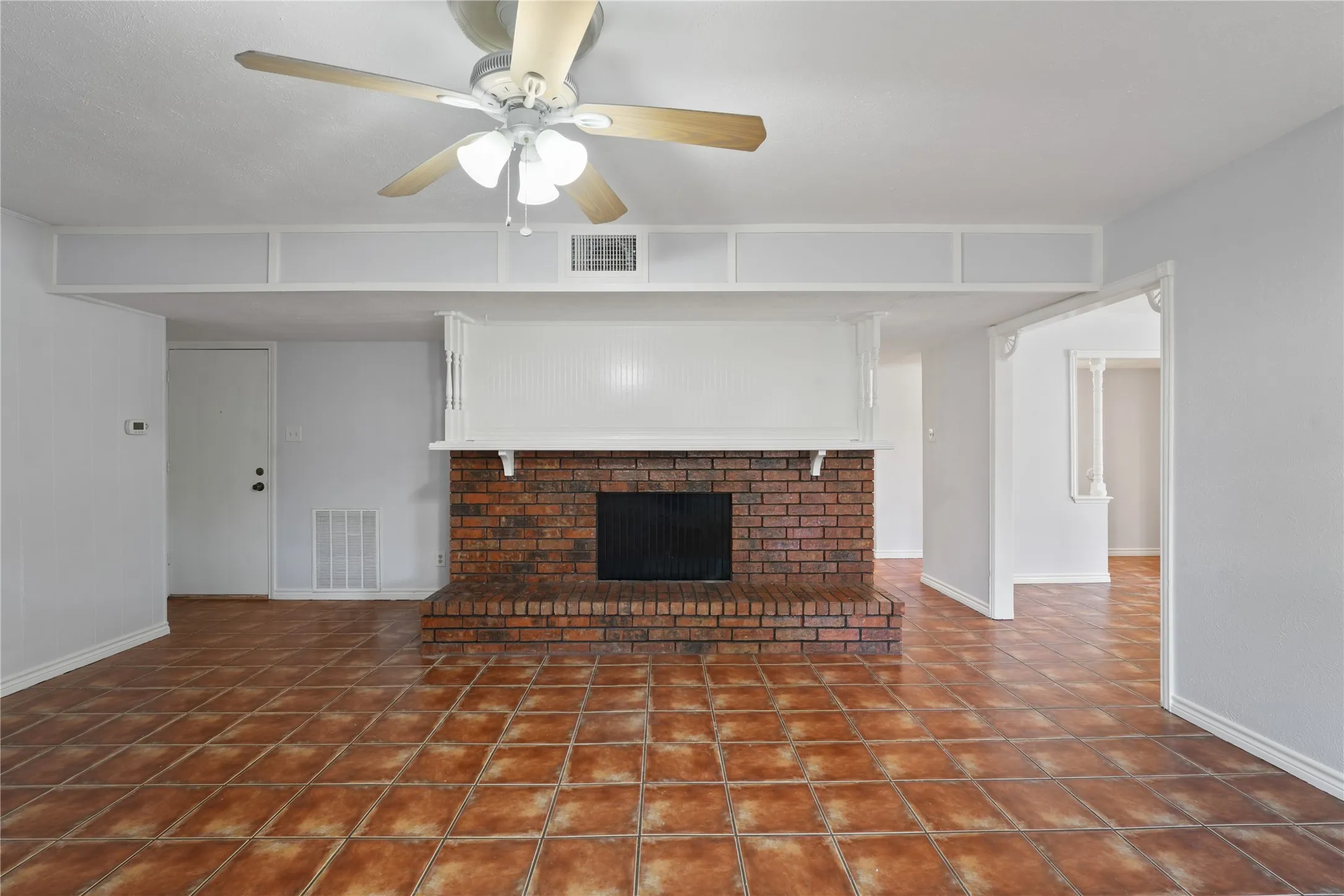 Unfurnished living room featuring dark tile floors, ceiling fan, and a brick fireplace