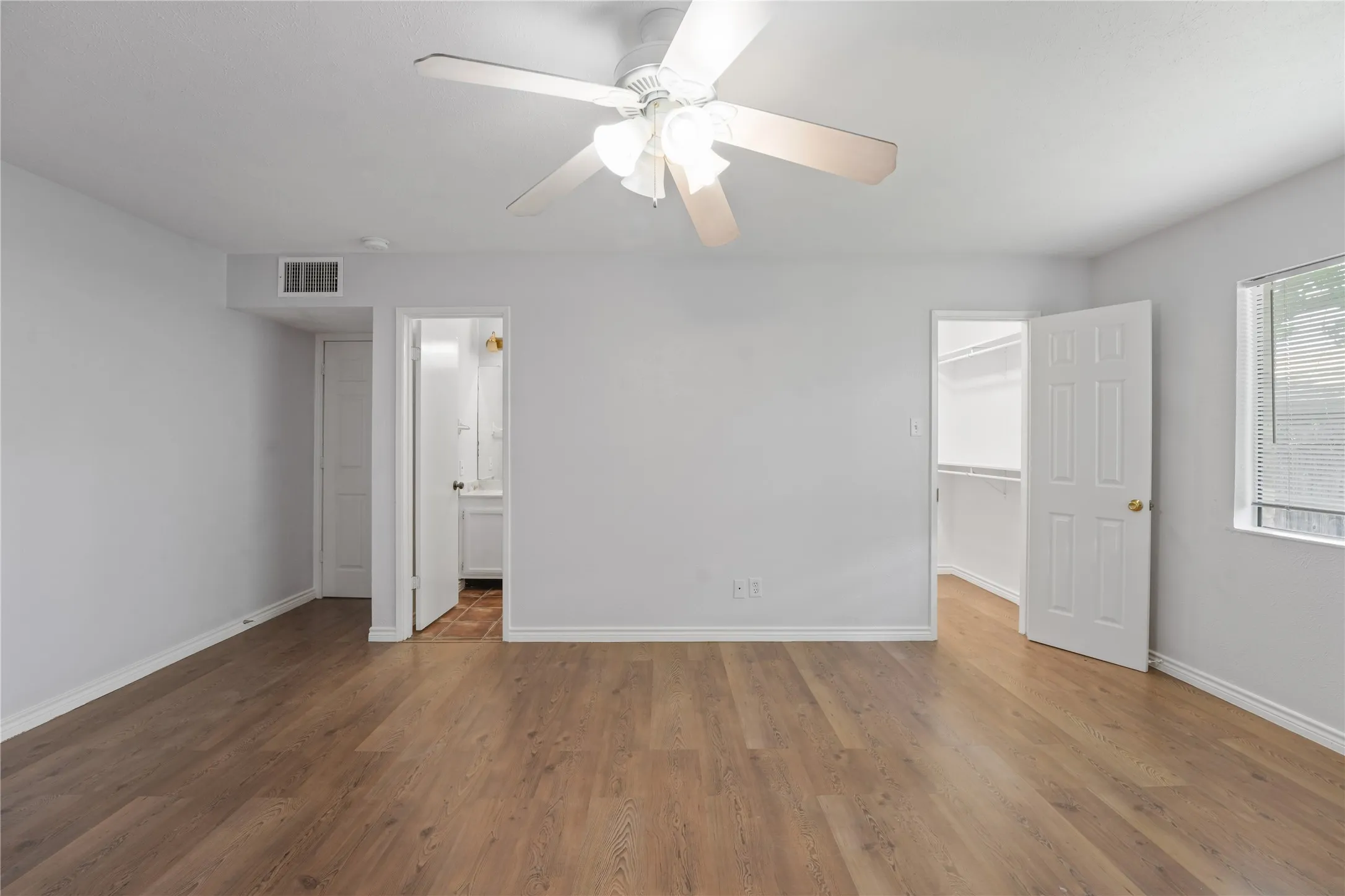 Unfurnished bedroom featuring wood-type flooring, ceiling fan, a walk in closet, and ensuite bathroom