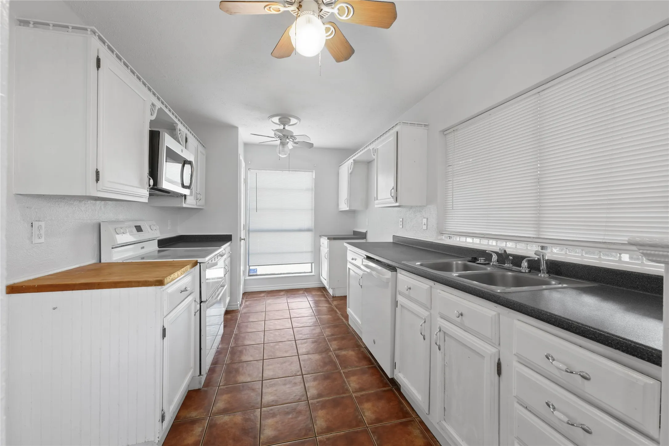 Kitchen with white cabinetry, dark tile floors, ceiling fan, and white appliances