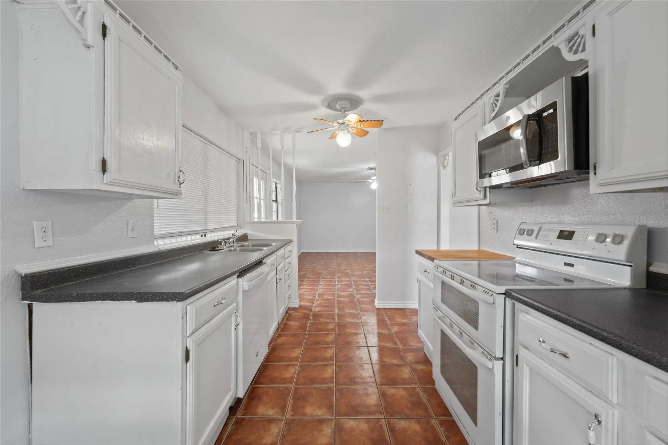 Kitchen with ceiling fan, dark tile floors, white cabinets, sink, and white appliances