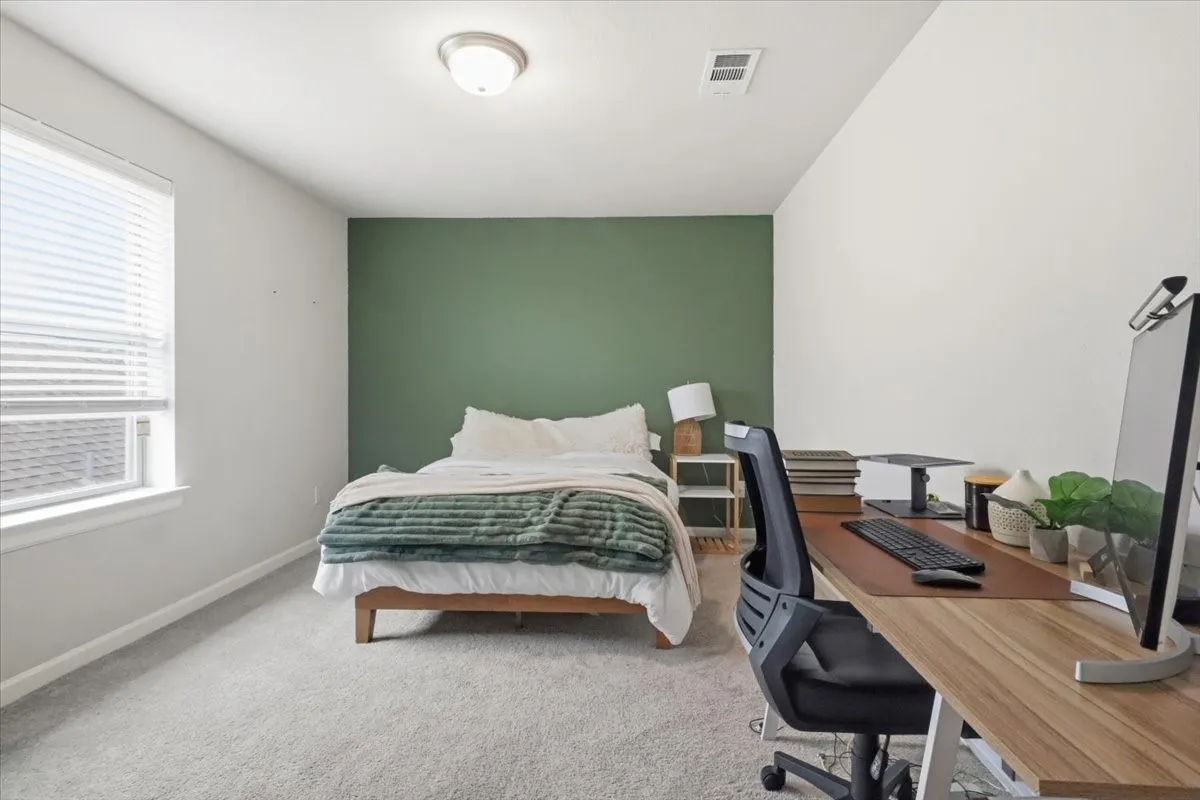 Plush carpeting, a prominent window with blinds, a contrasting accent wall, and a flush mount ceiling light fixture