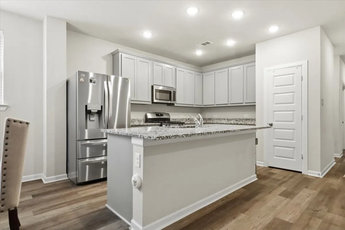 Kitchen featuring wood-finish flooring, recessed lighting, light-toned cabinetry, stainless steel appliances, and a kitchen island with a stone-finish countertop