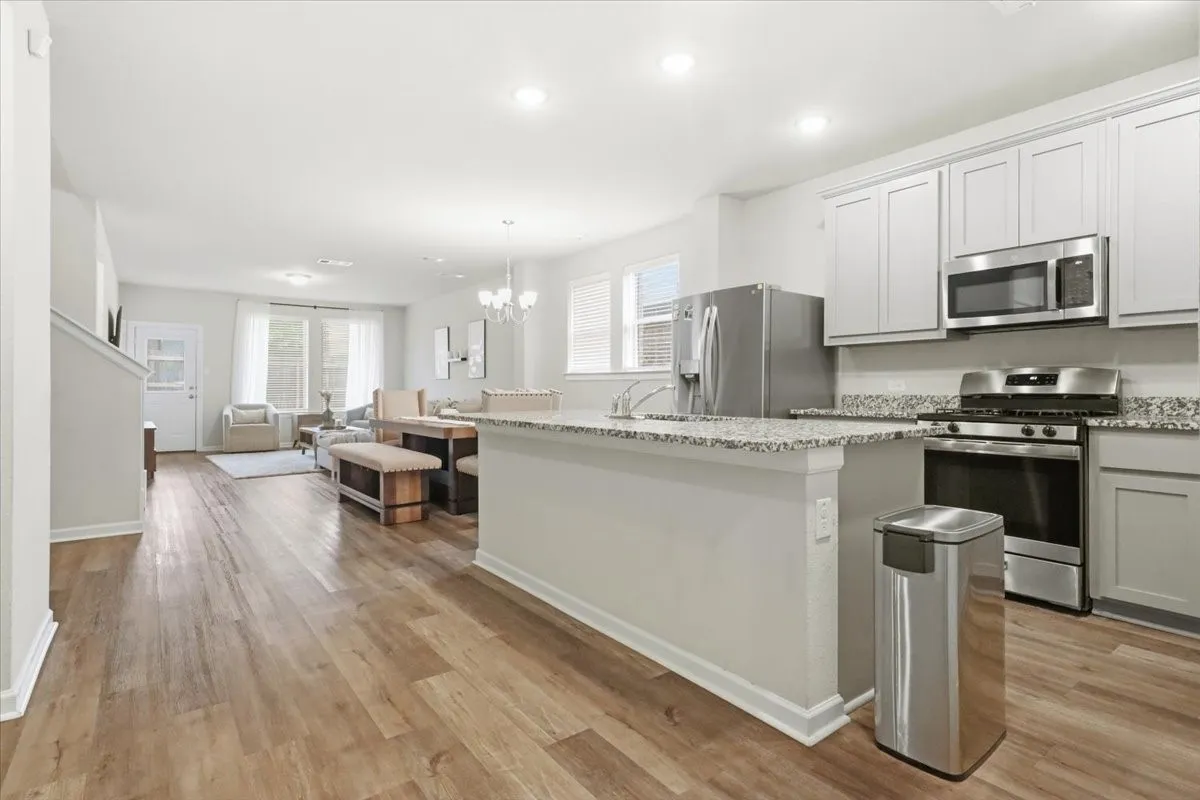 Open-concept kitchen and living area featuring wood-finish flooring, light gray cabinetry, stainless steel appliances, and granite countertops