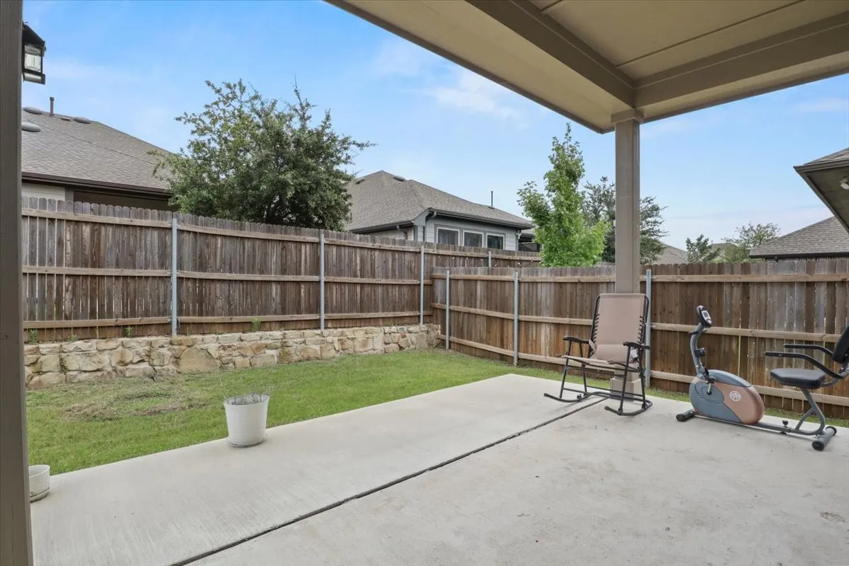 Covered concrete patio with a wood privacy fence and stone retaining wall