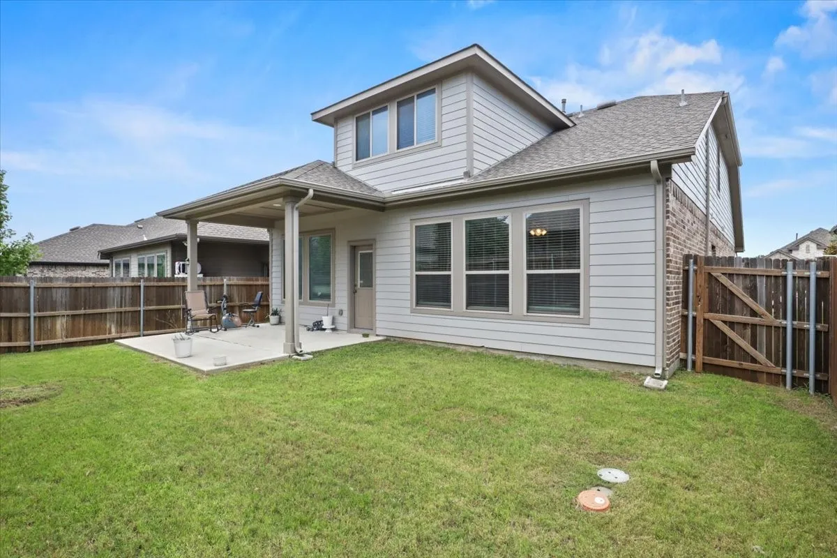 Expansive grass lawn with a covered concrete patio, privacy fencing, and exterior siding