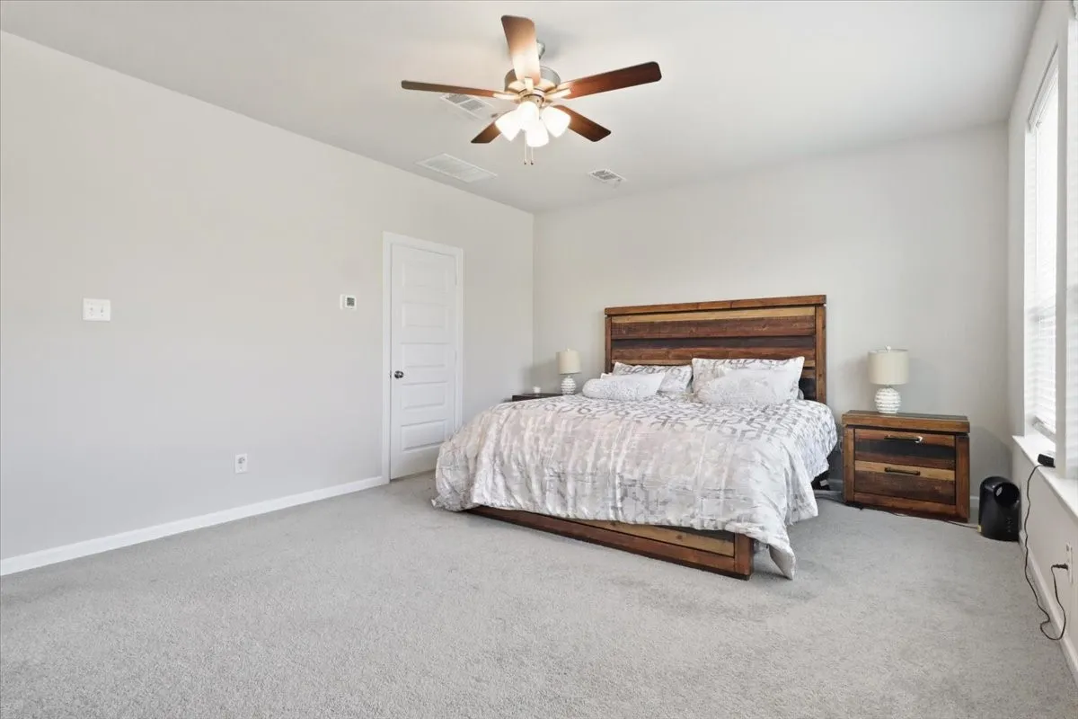 Ceiling fan with light fixture, light gray carpeting, white paneled door, and multiple windows with blinds