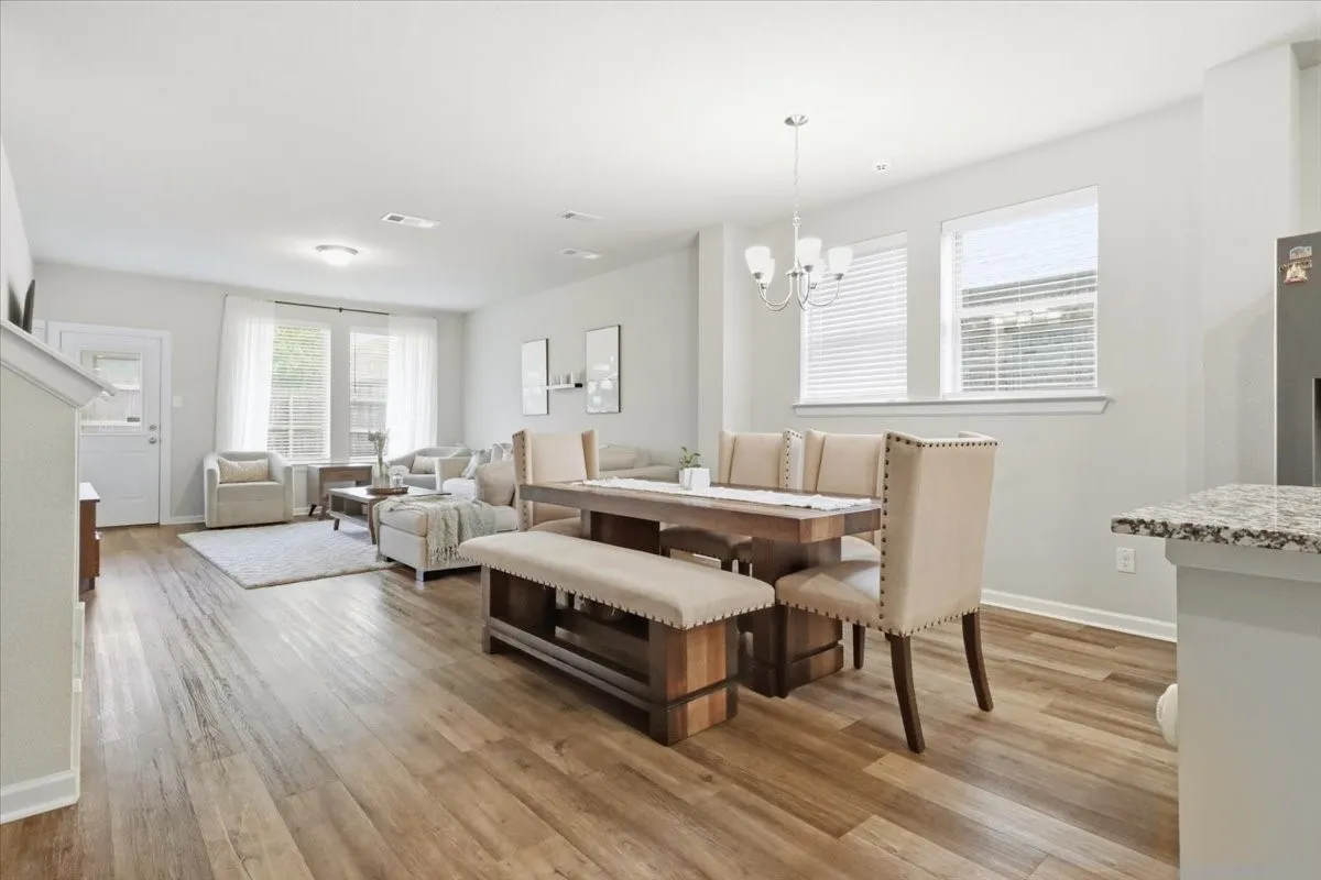Open-concept living space featuring wood-finish flooring, a dining area with a chandelier, and multiple windows