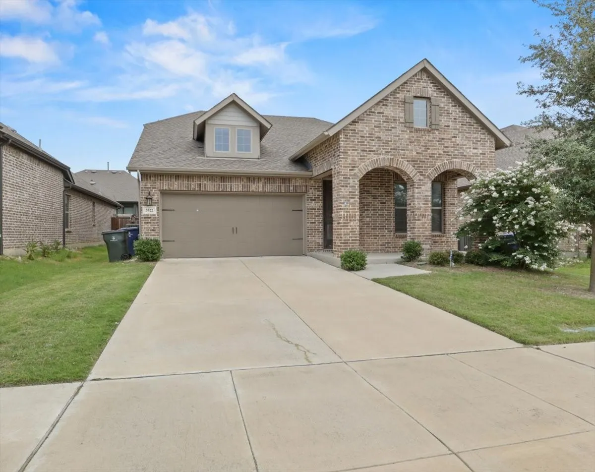 Brick facade with arched entry, attached two-car garage, dormer window, and concrete driveway