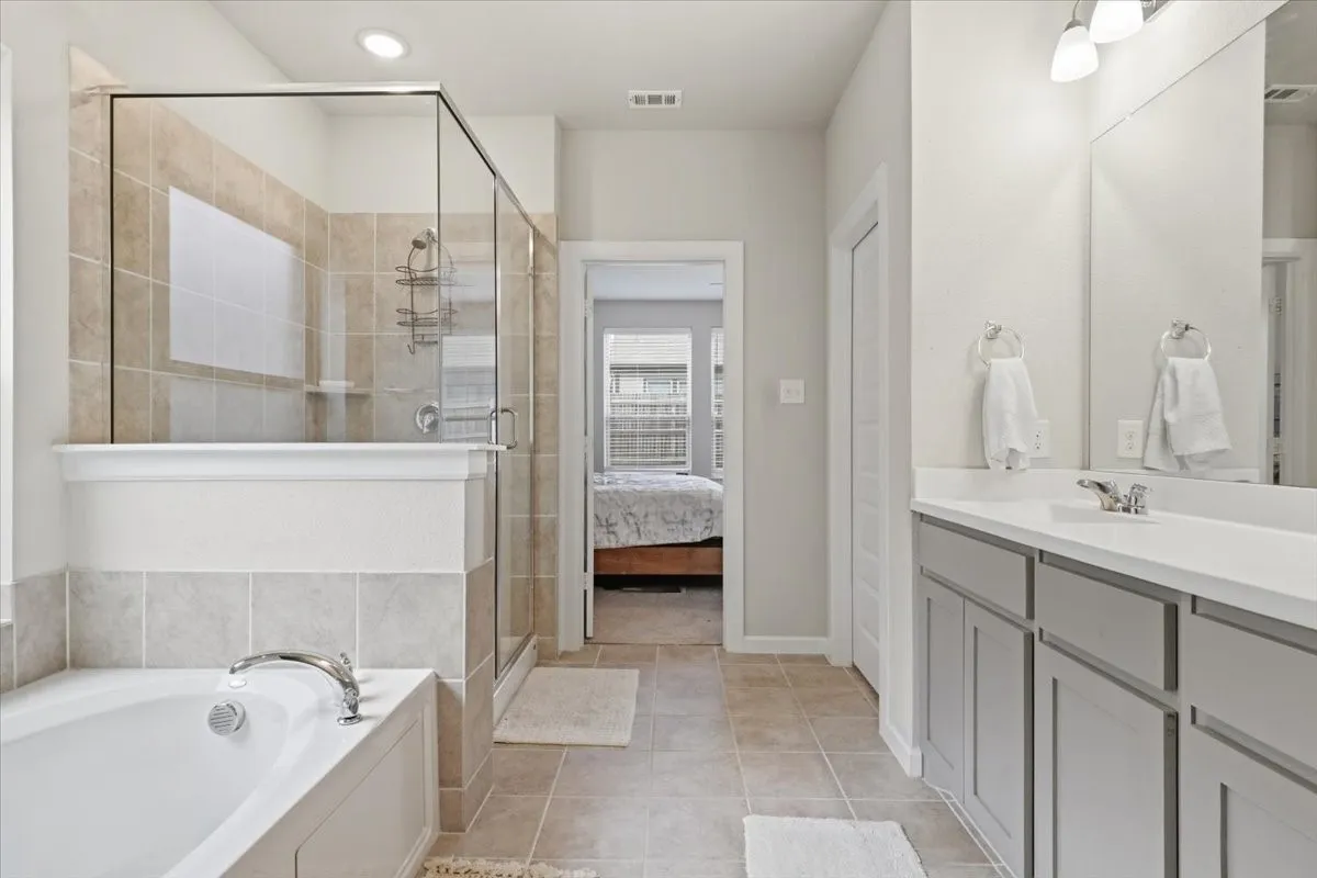 Tiled flooring with a built-in soaking tub, a separate glass-enclosed shower with tiled surround, and a vanity with a single basin and integrated lighting